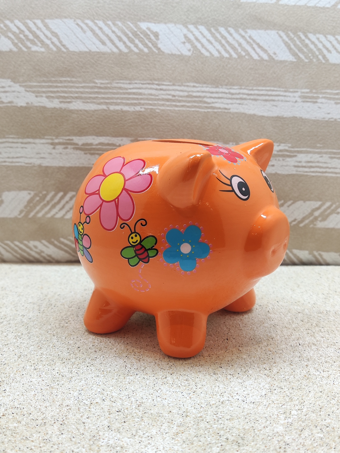 Cofrinho de cerâmica laranja decorado com flores e abelhas coloridas.