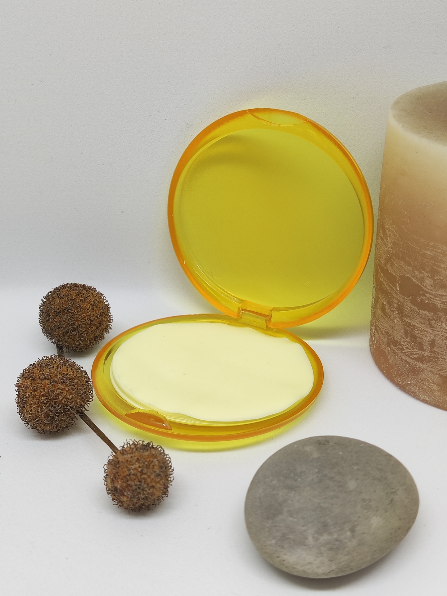 Estojo amarelo aberto com disco creme e elementos naturais ao redor