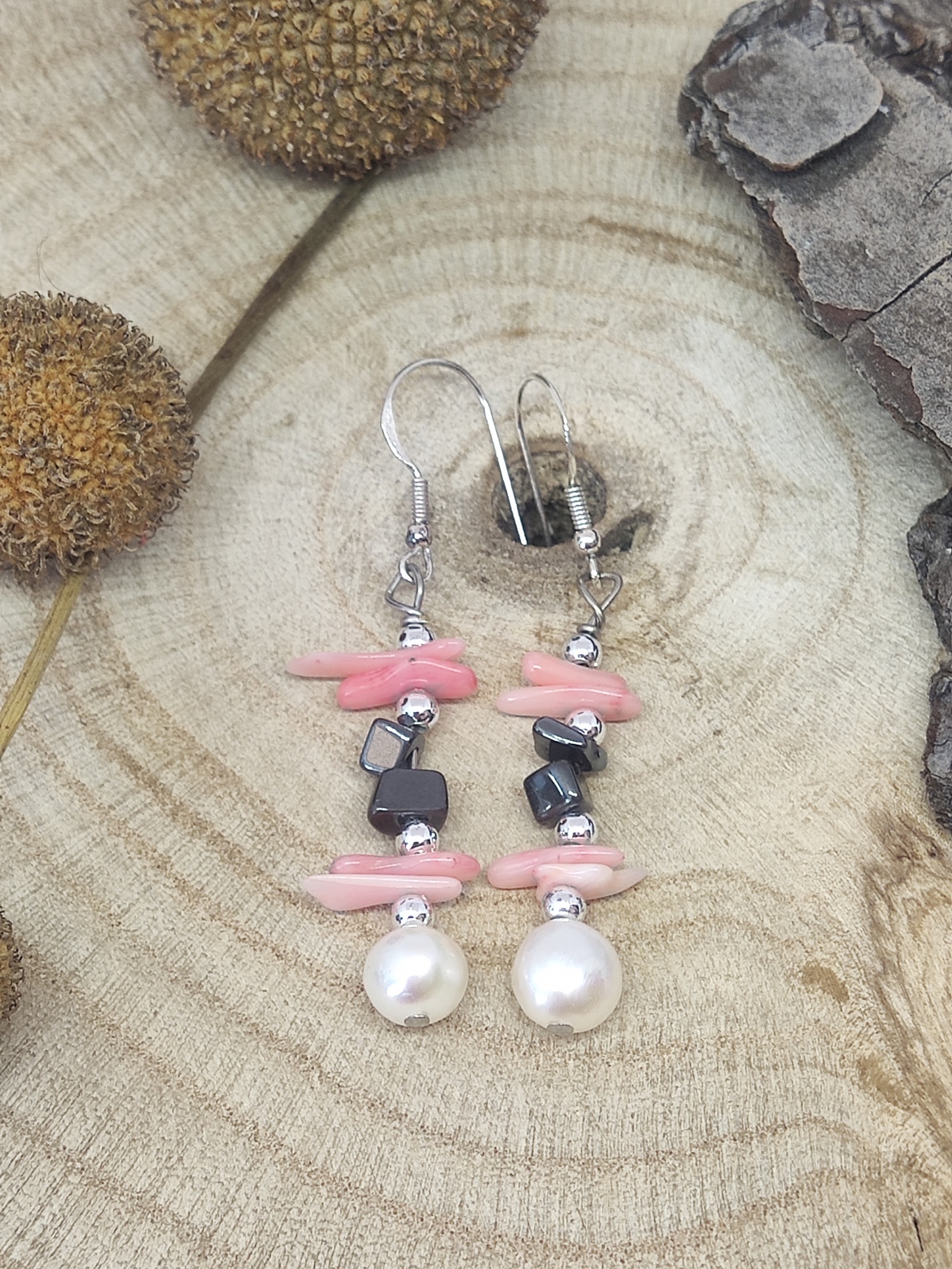 Brincos pendentes com pedras cor-de-rosa, contas prateadas, pedras pretas e pérolas sobre superfície de madeira