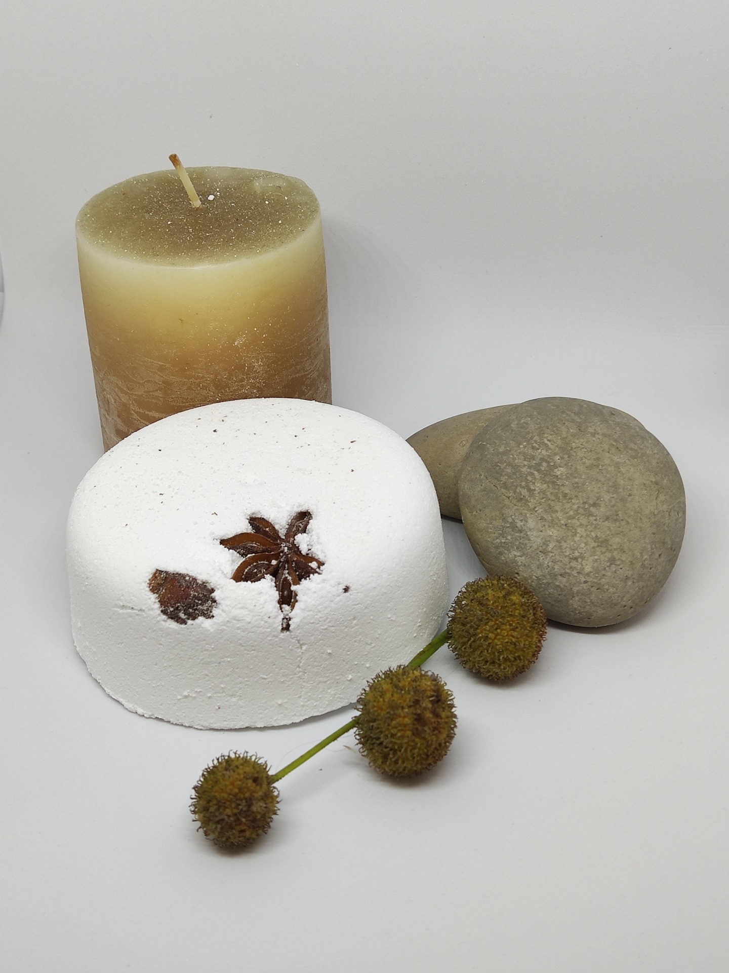 Vela marrom, bloco branco com especiarias, dois seixos e frutos secos sobre fundo branco