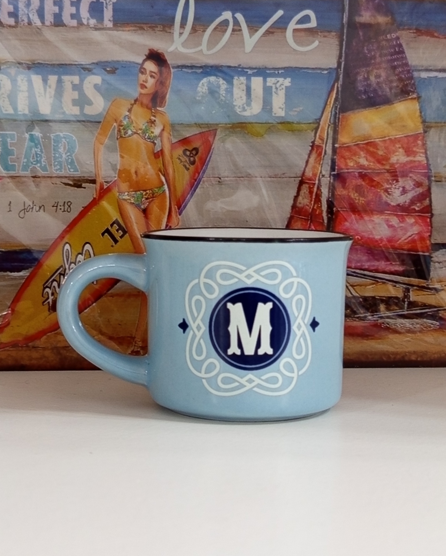 Caneca azul clara com letra M branca em círculo azul sobre fundo colorido