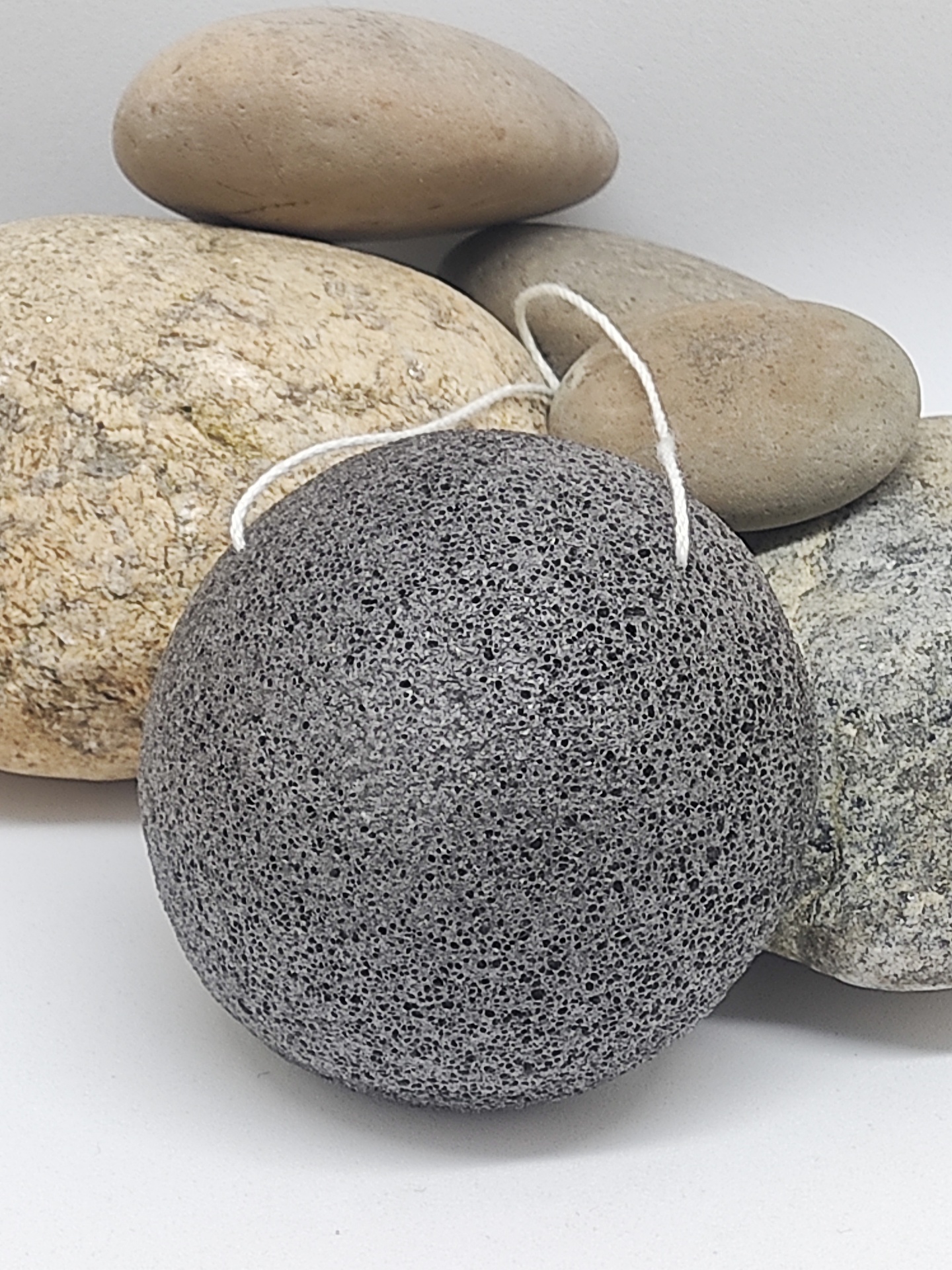 Esfregão esponja cinzento poroso com cordão branco diante de pedras