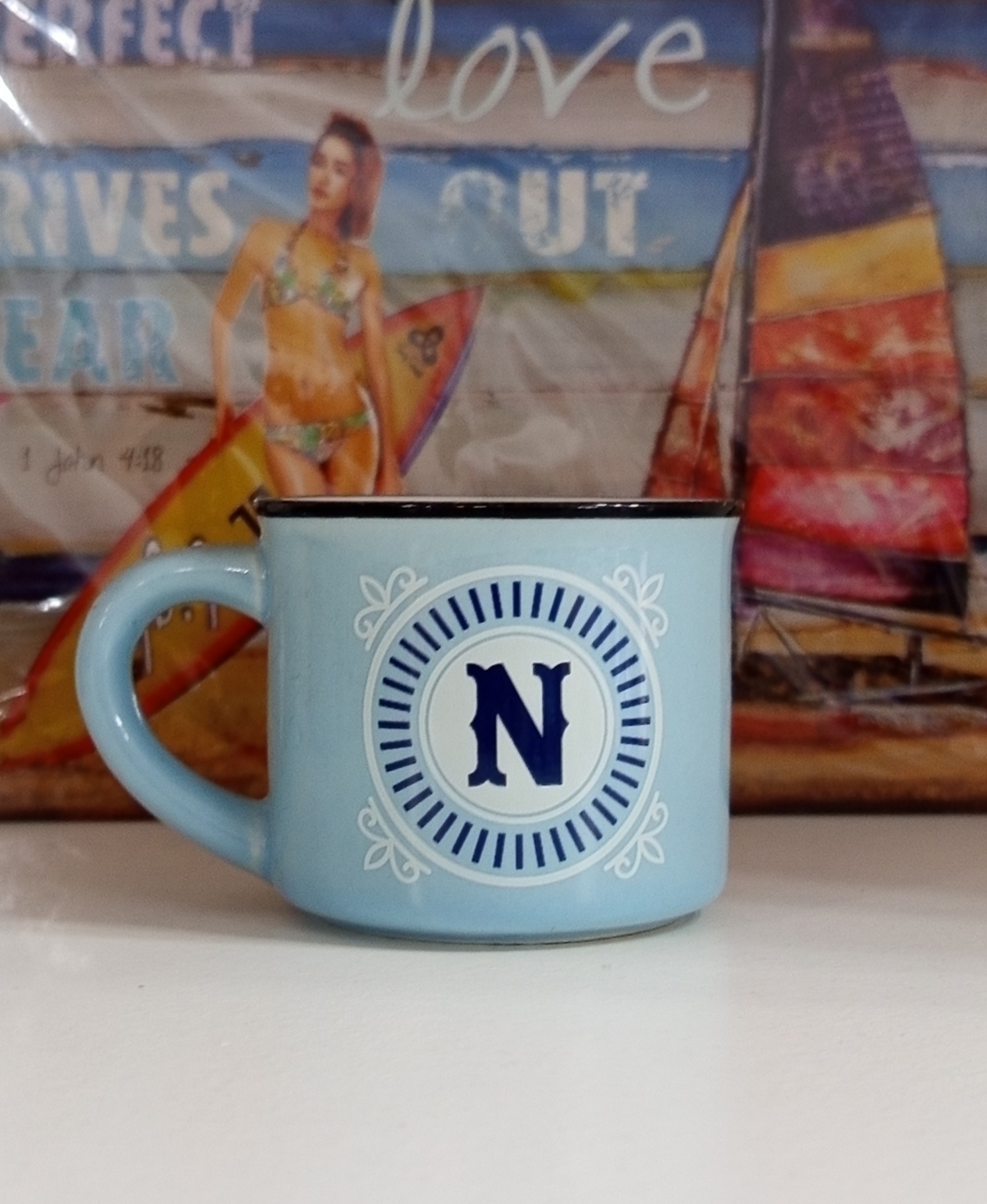Caneca azul com letra N em círculo, superfície branca e fundo colorido de praia