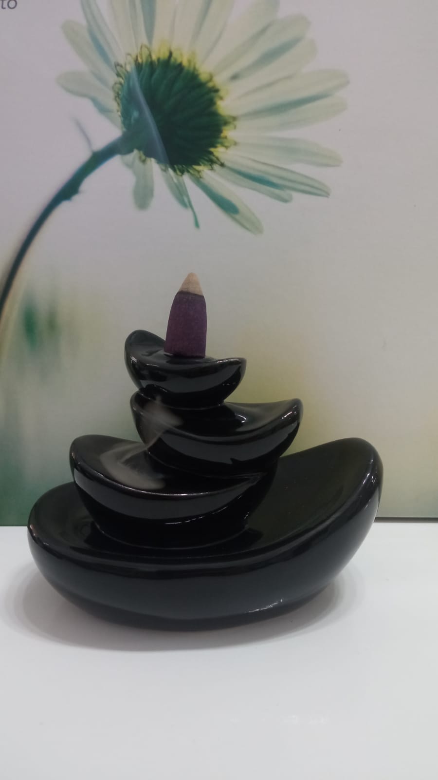 Incensário preto com cone de incenso roxo e fundo de flor branca