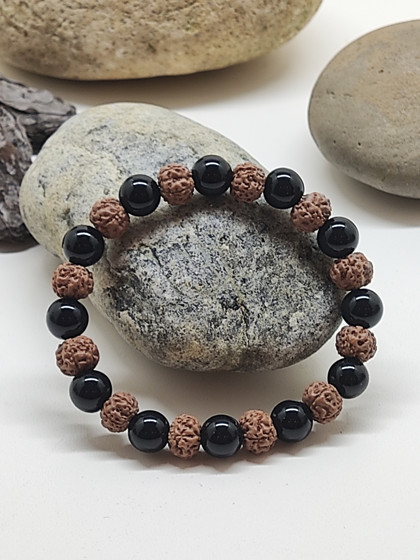 Pulseira com contas negras e castanhas sobre pedras cinzentas