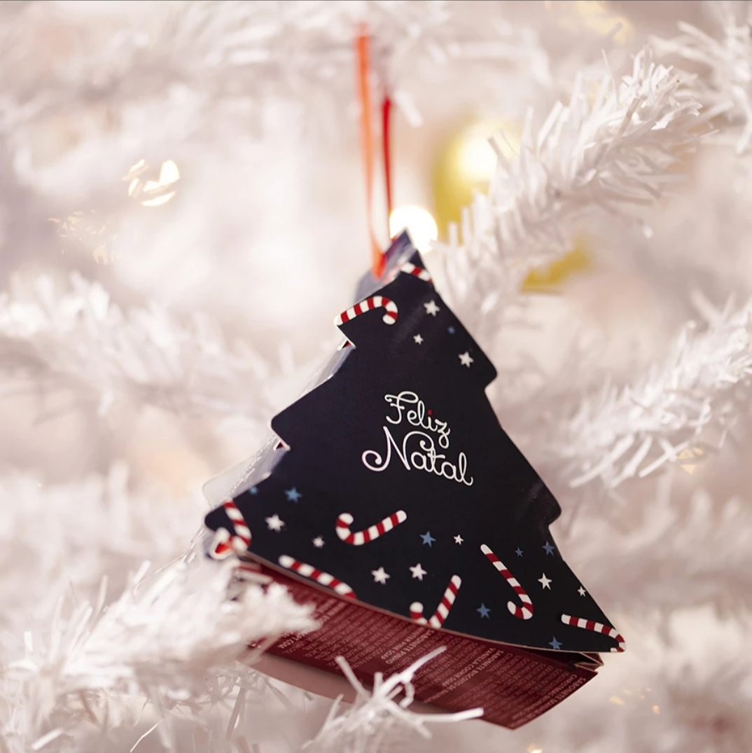 Ornamento de árvore de Natal preto com texto 'Feliz Natal' pendurado numa árvore branca