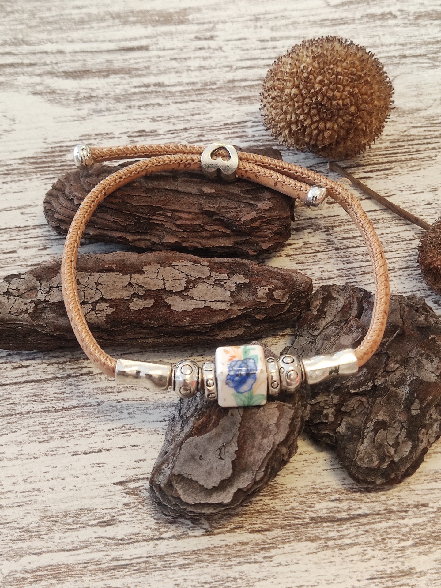 Pulseira com cordão bege e conta com padrão floral azul