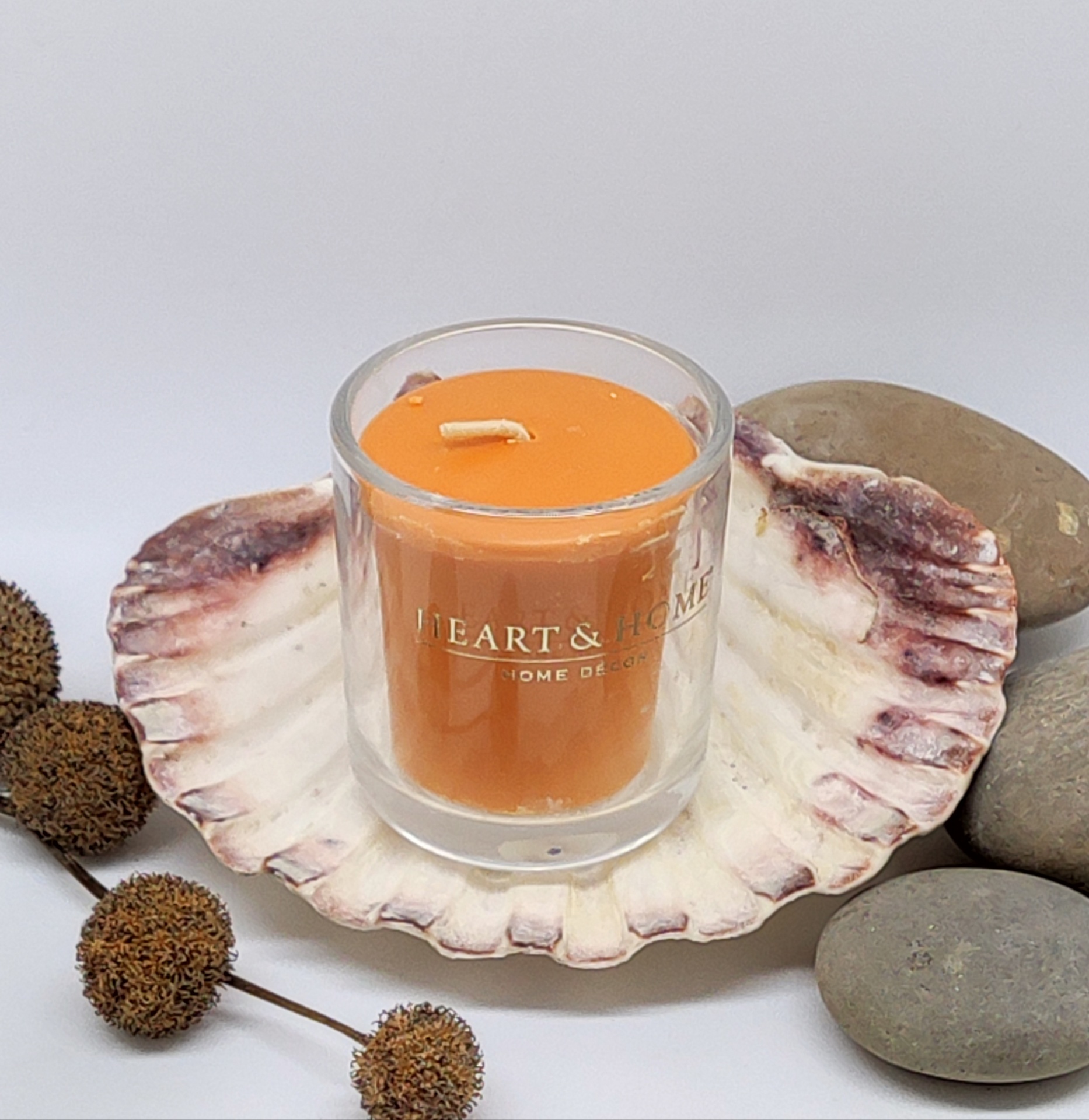 vela laranja em copo de vidro sobre concha rodeada por pedras e frutos secos