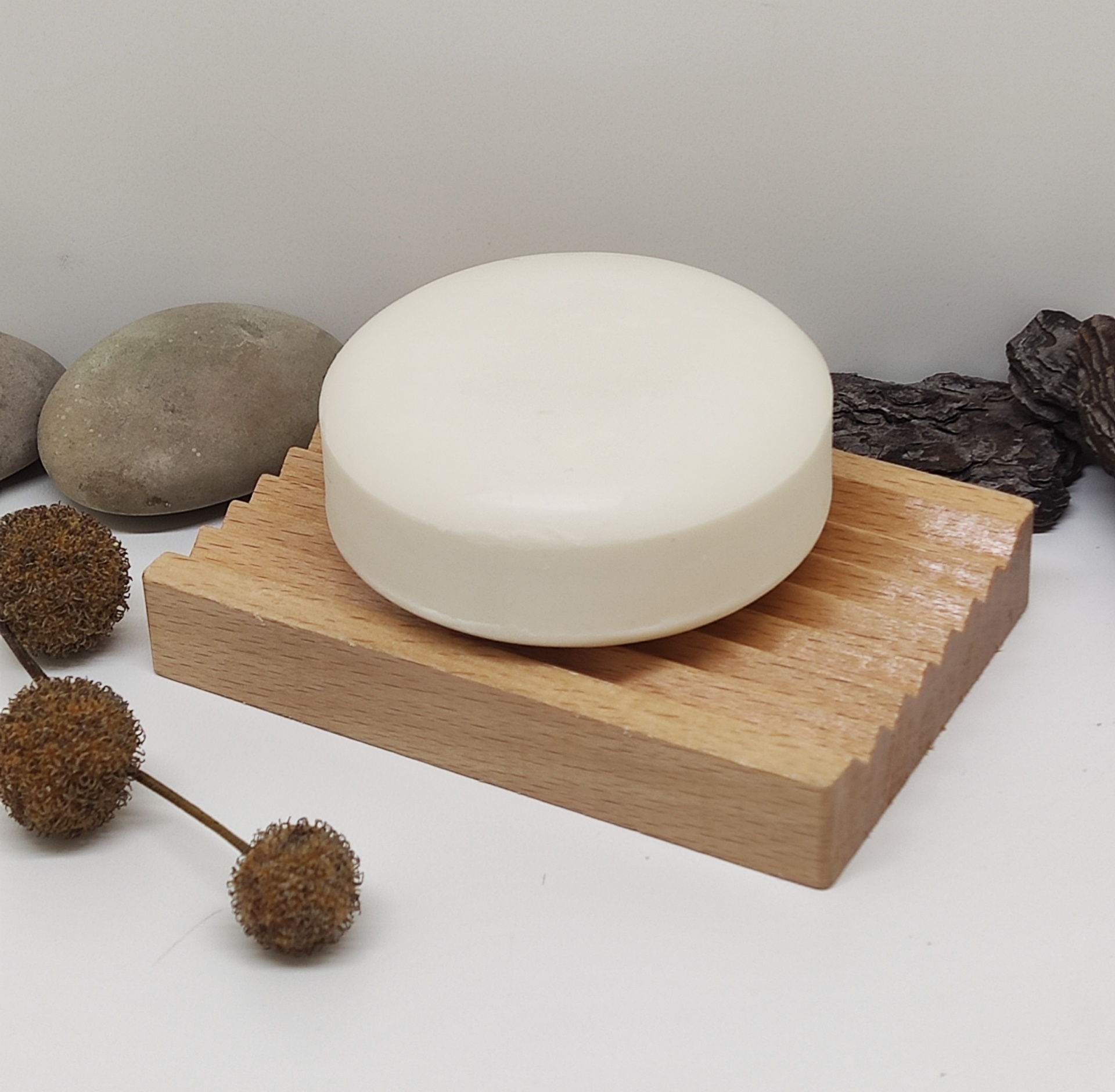 Sabonete branco redondo numa base de madeira com pedras e flores secas à volta