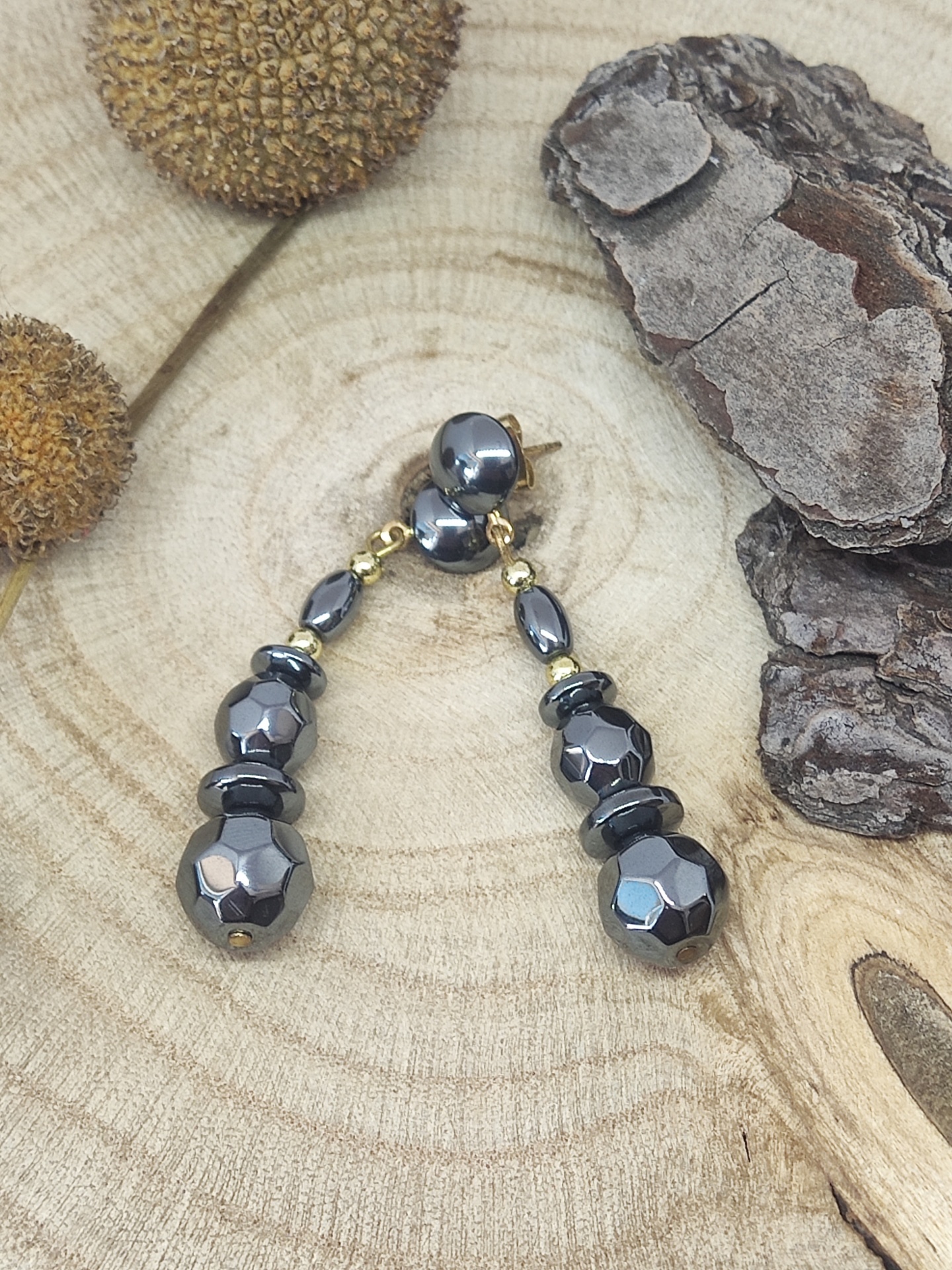 Brincos pretos facetados com detalhes dourados numa superfície de madeira rústica