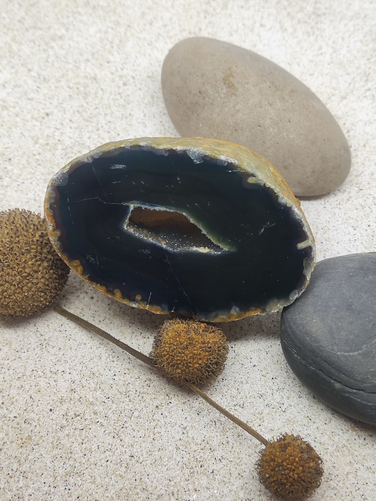 Seixos decorativos com geodo e ramos secos sobre superfície clara