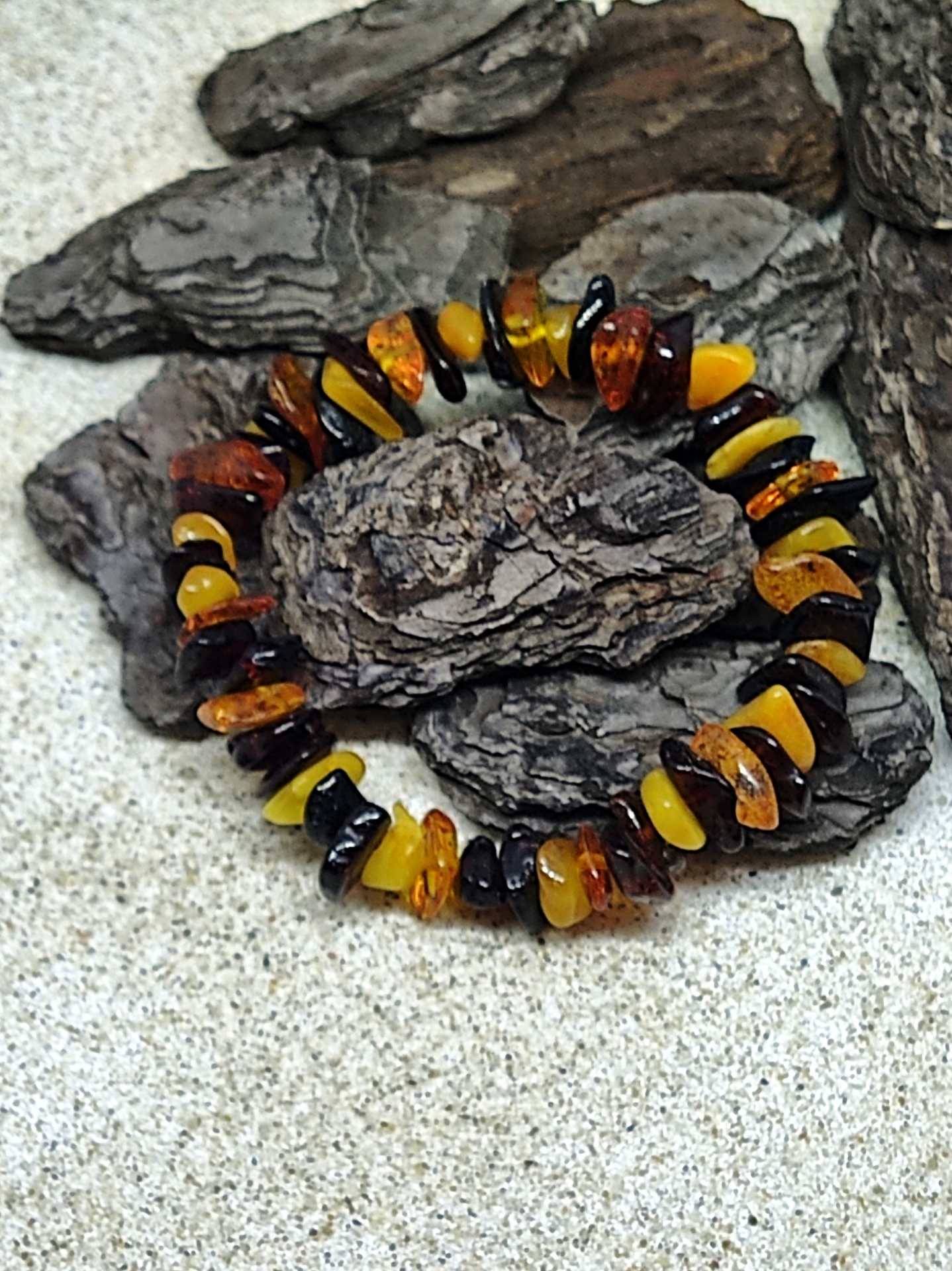 Pulseira de pedras de âmbar em tons castanho, amarelo e preto sobre cascas de árvore