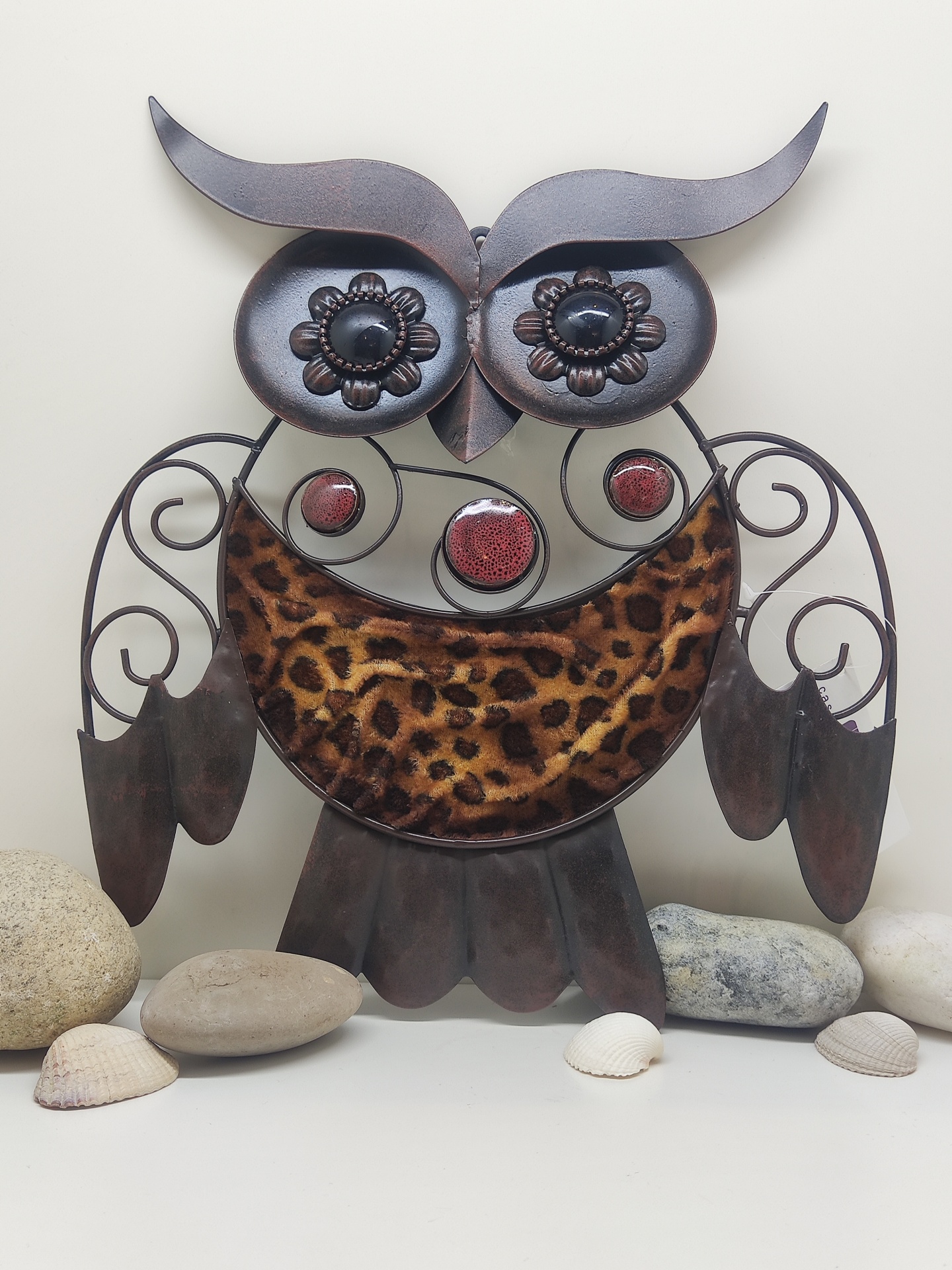 Escultura decorativa de coruja em metal com padrão de pelo e olhos decorados sobre superfície com pedras e conchas