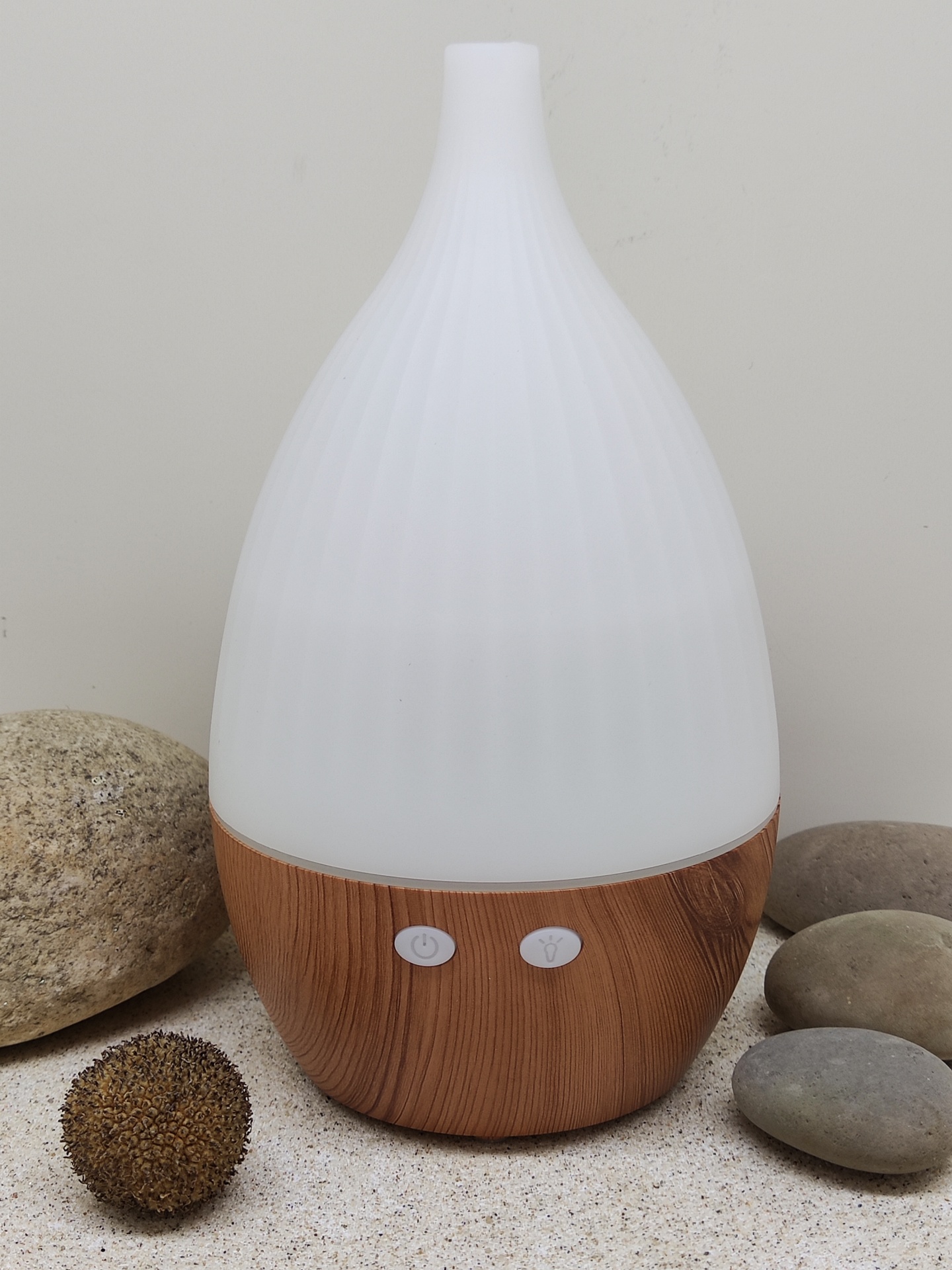 Difusor com base em madeira clara e parte superior branca texturizada em ambiente com pedras decorativas