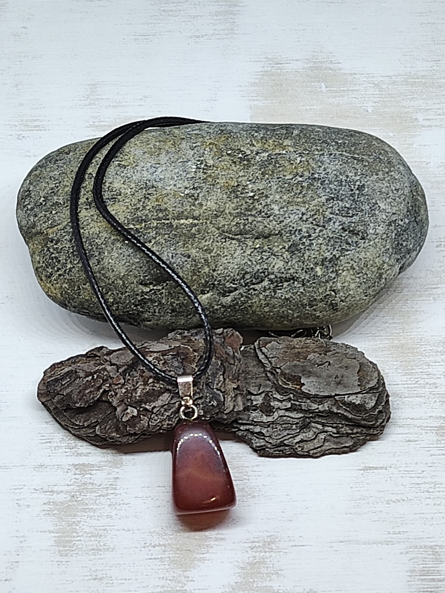 Colar com pendente em pedra polida castanha e cordão preto sobre pedra e casca de árvore