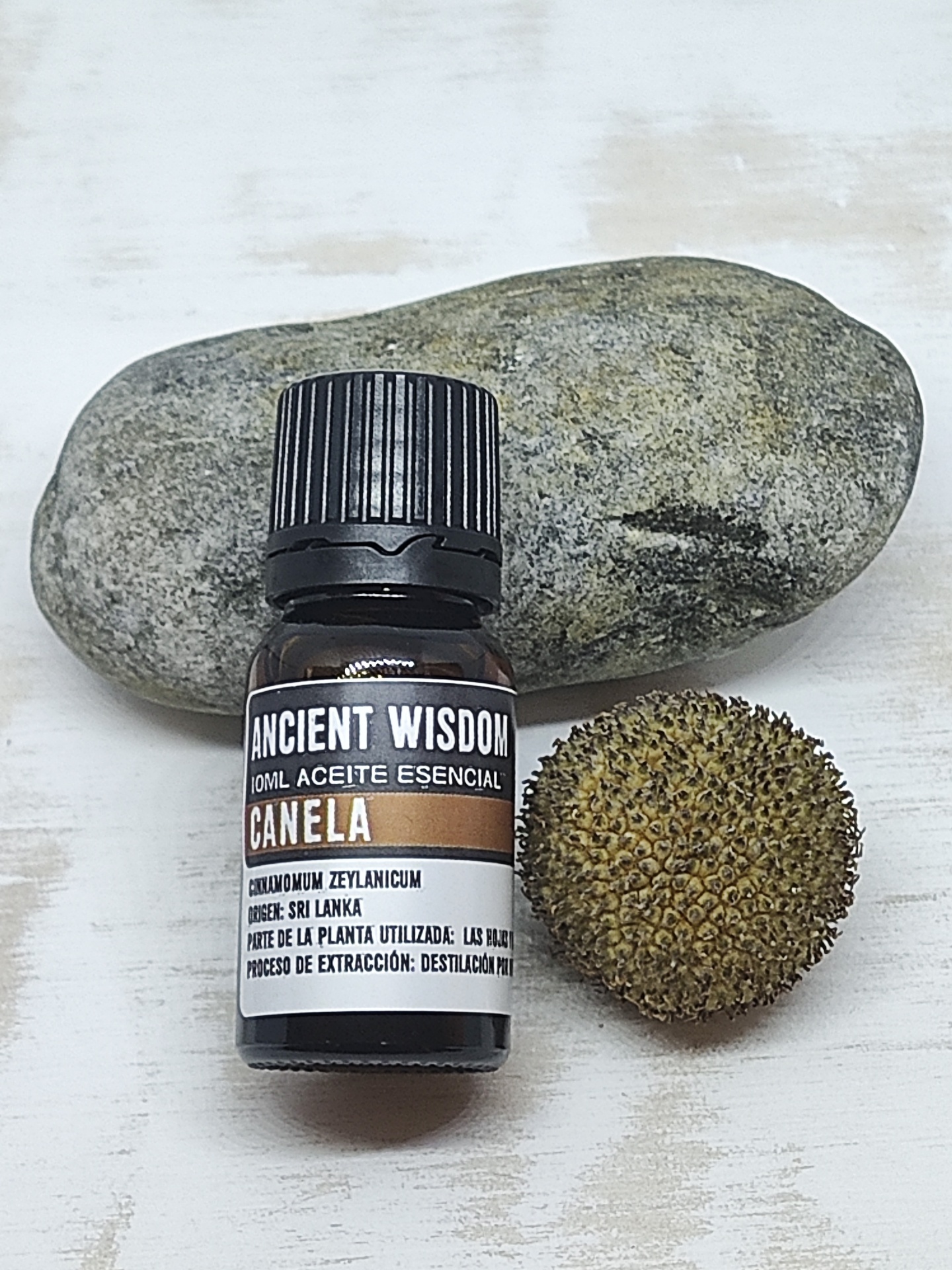 Frasco de óleo essencial de canela com uma pedra e uma baía ao lado, sobre uma superfície branca