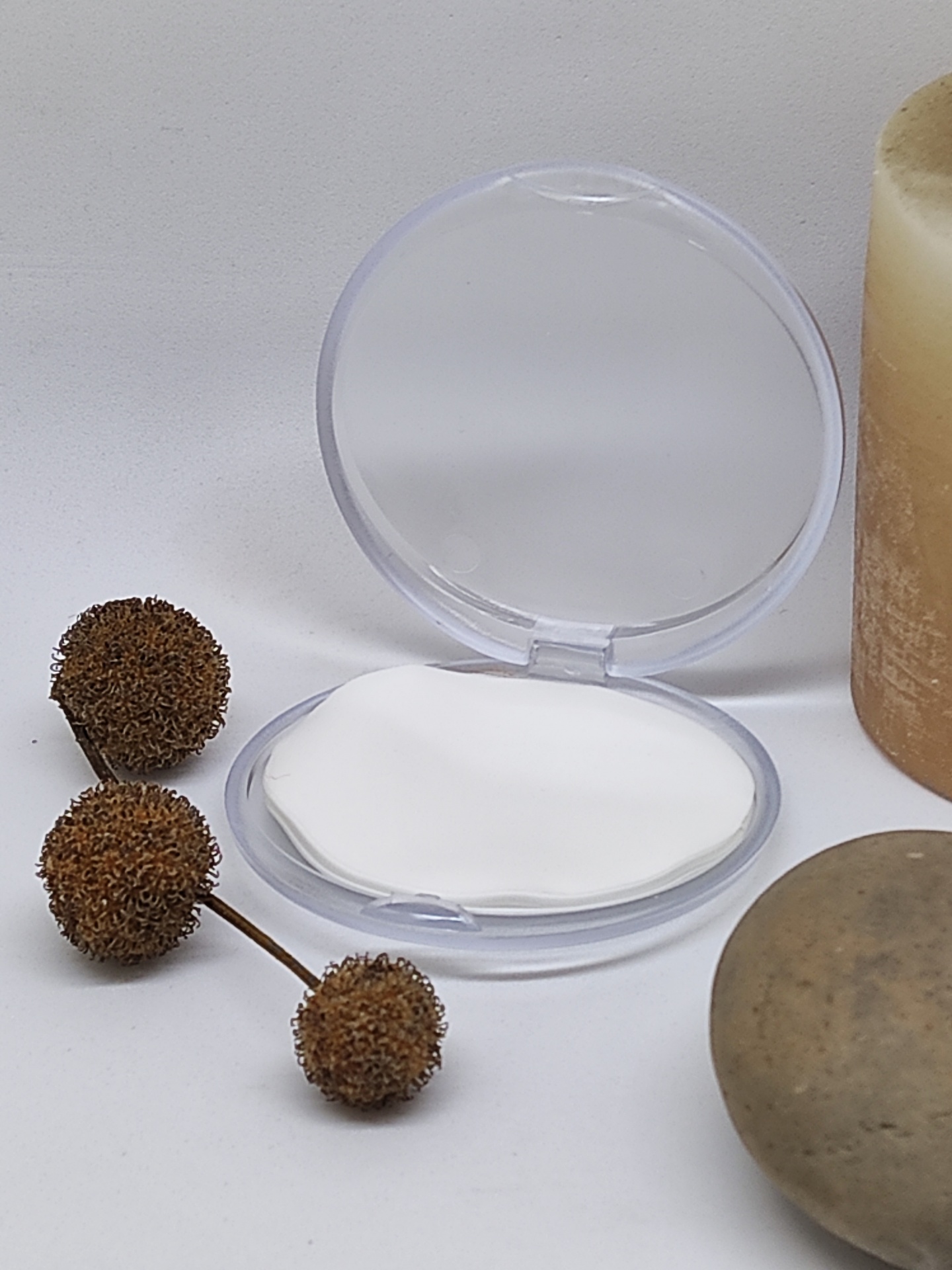 Compacto transparente com almofada branca, ramos secos, vela e pedra