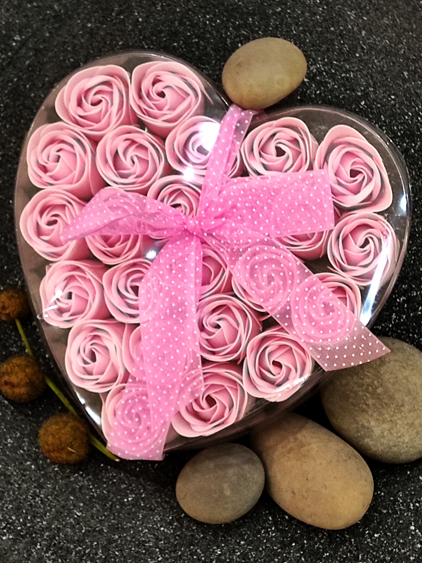 Caixa em forma de coração com rosas cor de rosa e laço rosa sobre pedras
