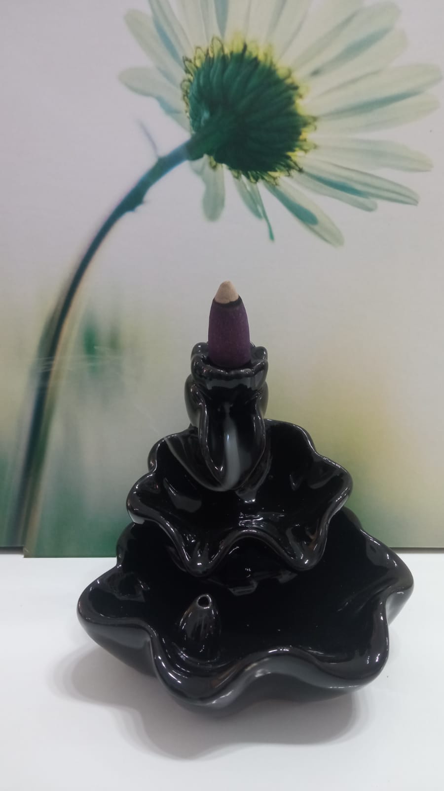 Incensário cerâmico preto com cone de incenso roxo e fundo de flor branca desfocada