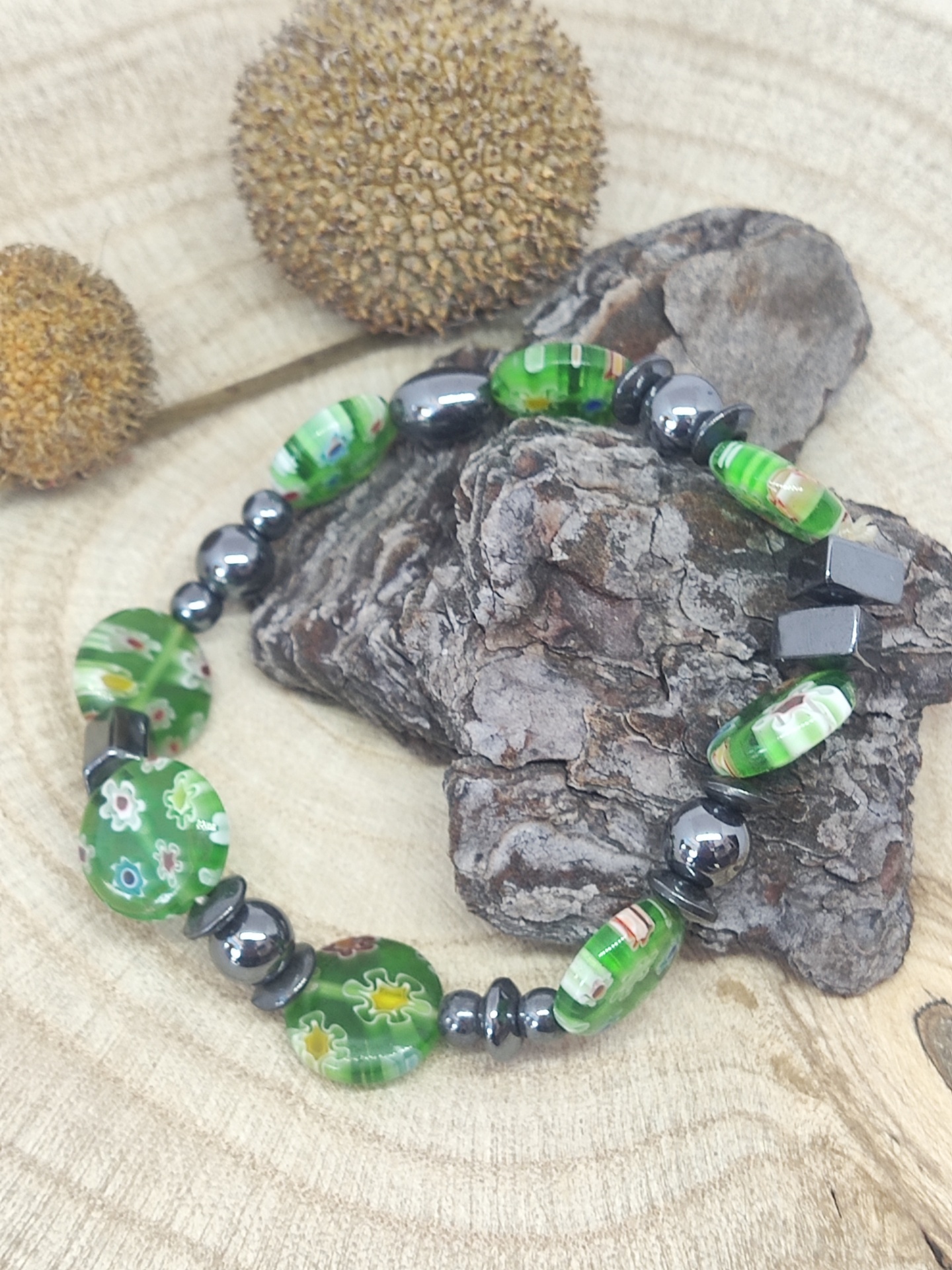 Pulseira verde com contas de vidro e metálicas sobre casca e madeira
