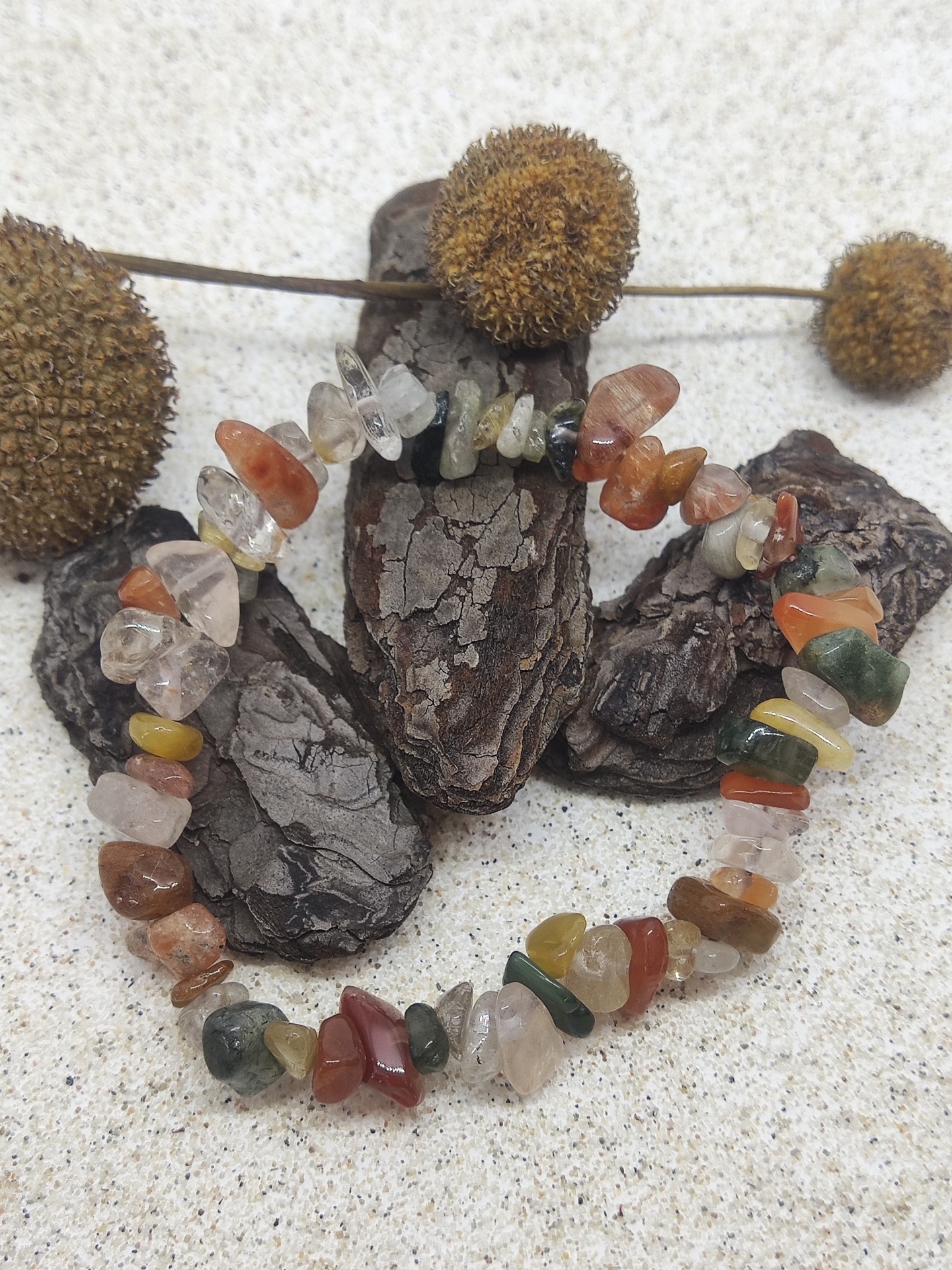 Bracelete de pedras semipreciosas multicoloridas sobre casca e fundo de areia com flores secas