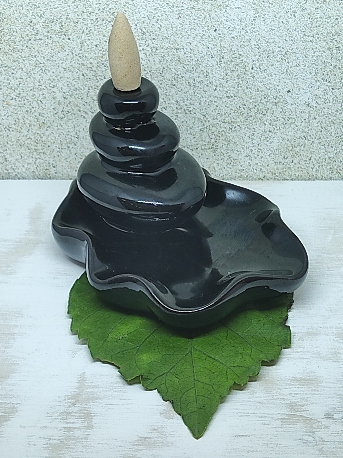 Incensário cerâmica preta com cone de incenso sobre folha verde