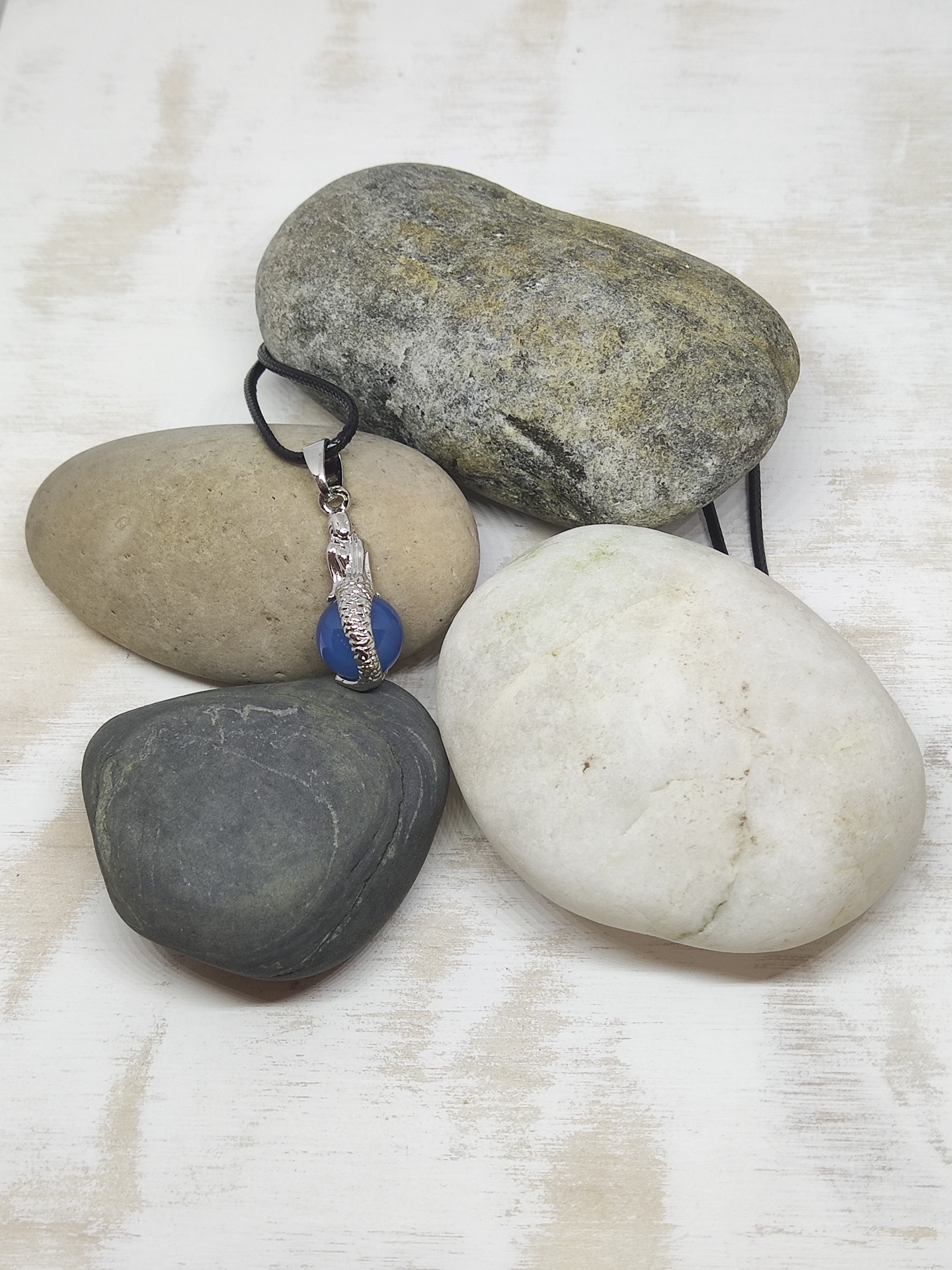 Quatro pedras de cores diferentes, uma com pendente metálico e fio preto.