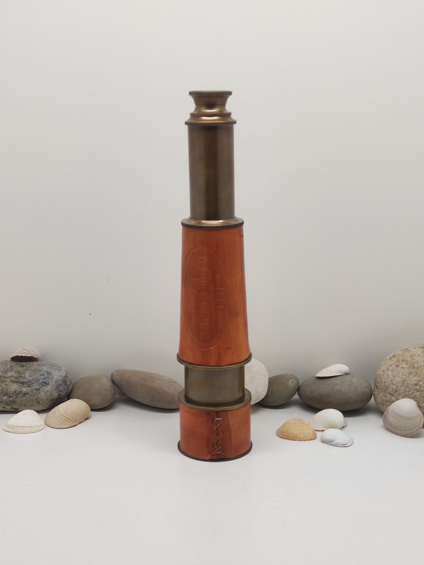 Cálice marítimo telescópico em latão e couro castanho rodeado por pedras e conchas