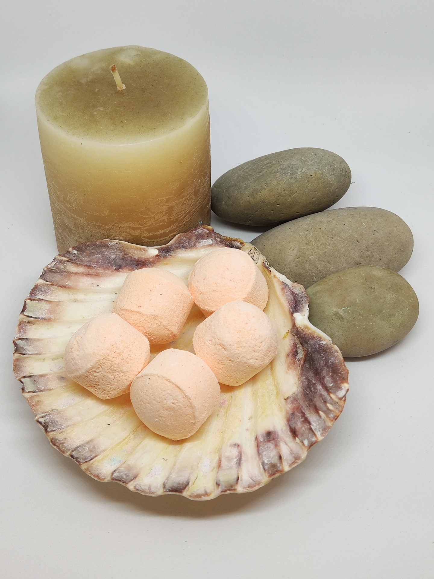 Sais de banho cor de pêssego em concha natural, vela bege e pedras lisas cinzentas