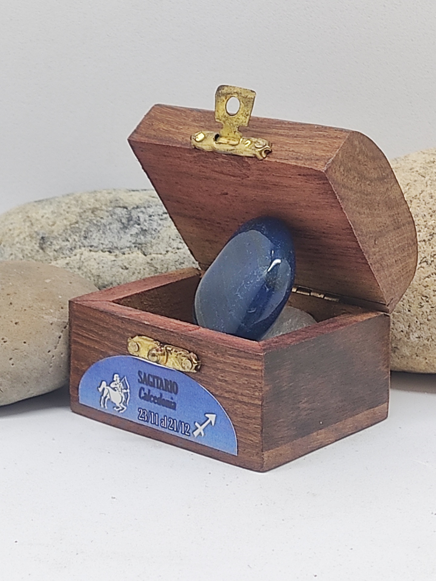Caixa de madeira com pedra azul polida e etiqueta azul com texto e símbolo de Sagitário