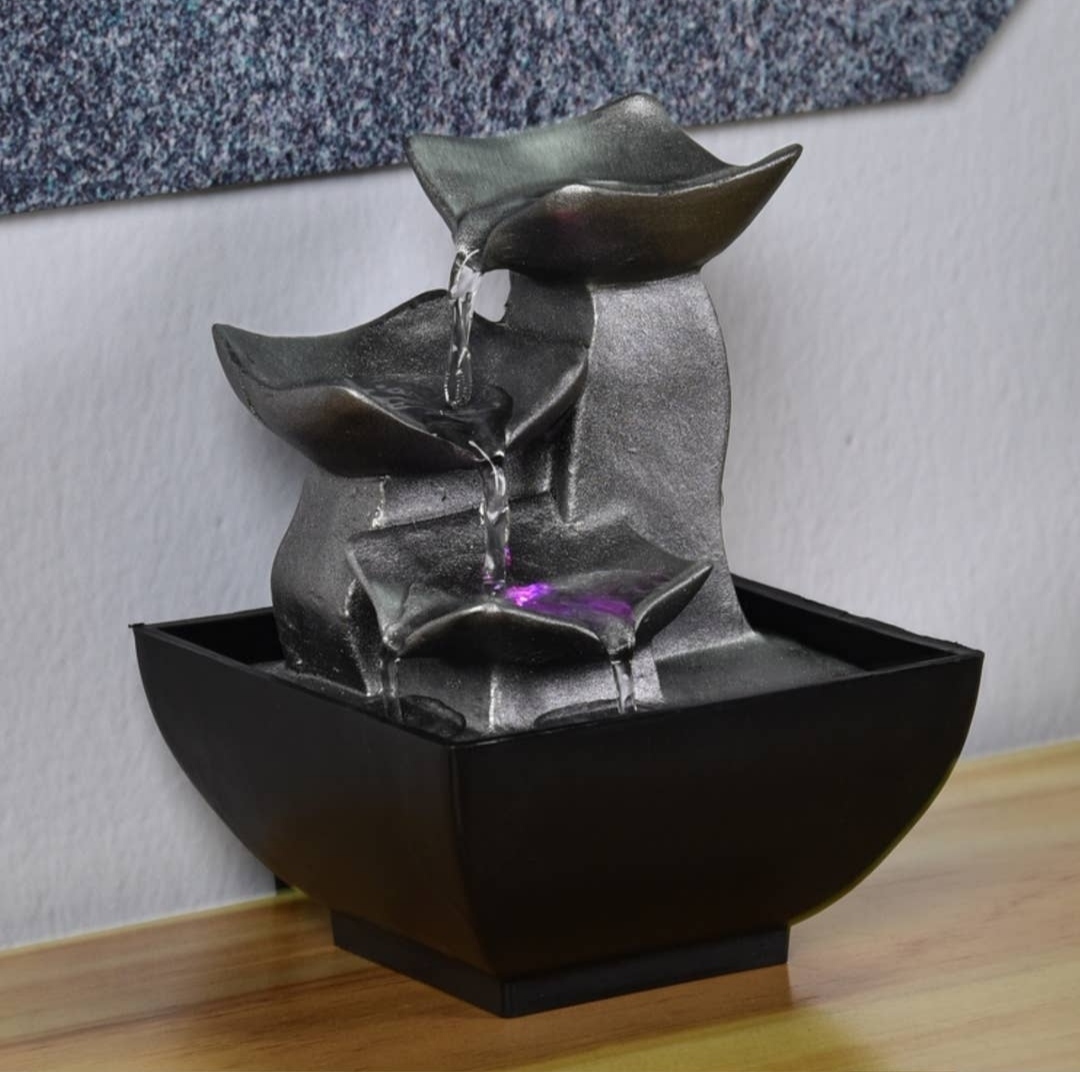 Fonte decorativa metálica com iluminação roxa, base preta quadrada