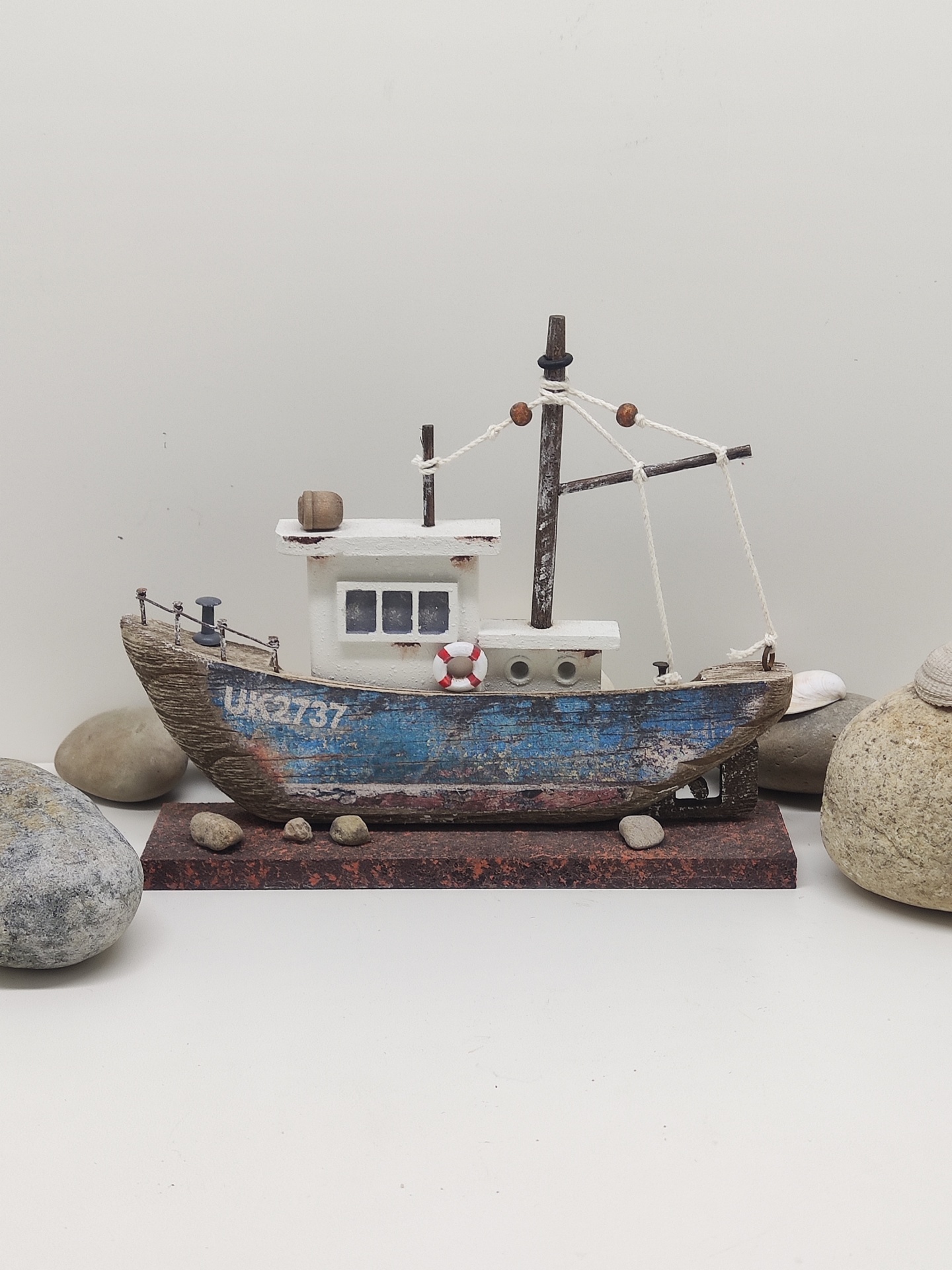 Modelo decorativo de barco de madeira azul e branco com detalhes e pedras ao redor