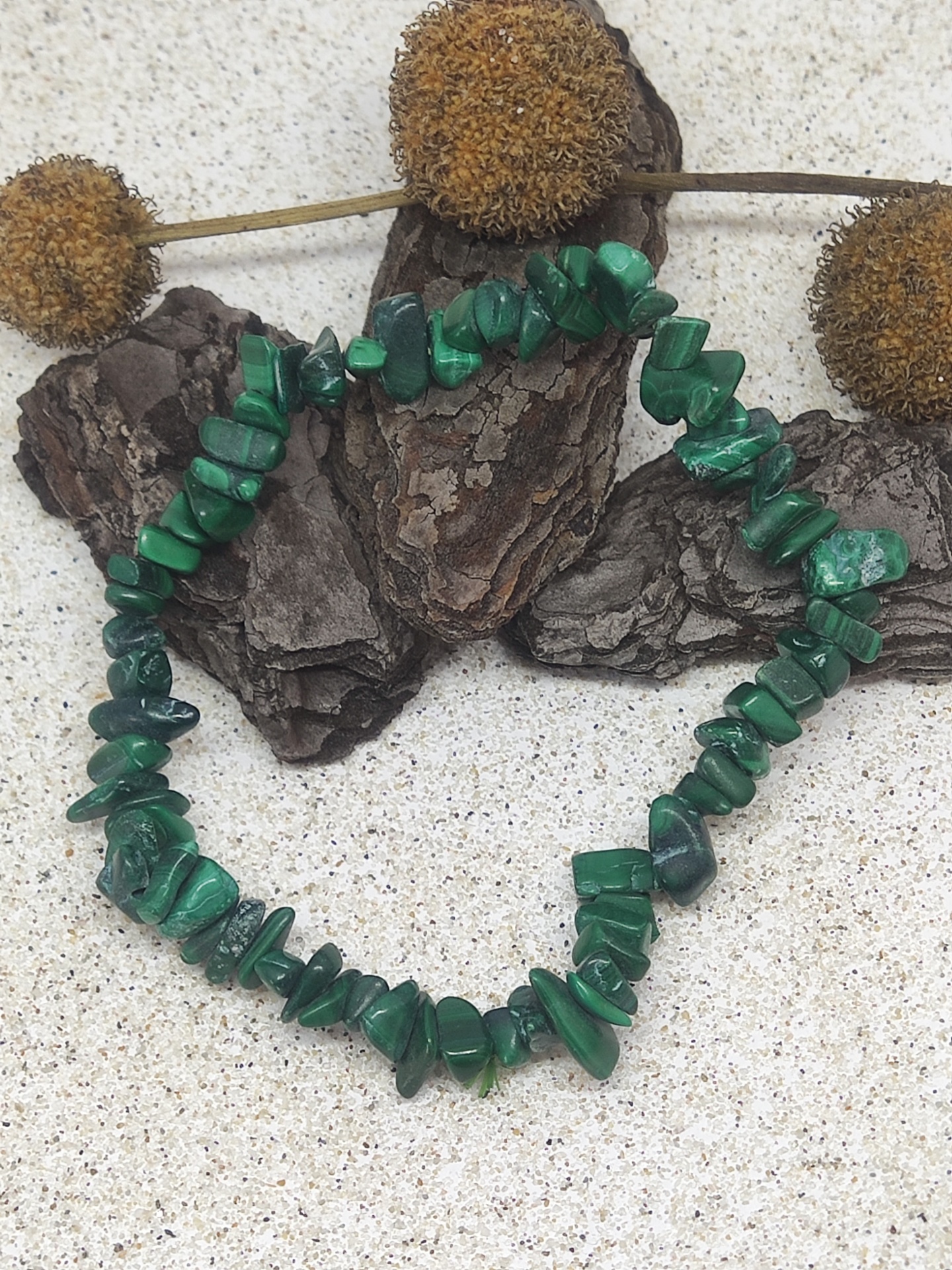 Pulseira verde de pedras irregulares sobre superfície clara com casca de árvore e flores secas