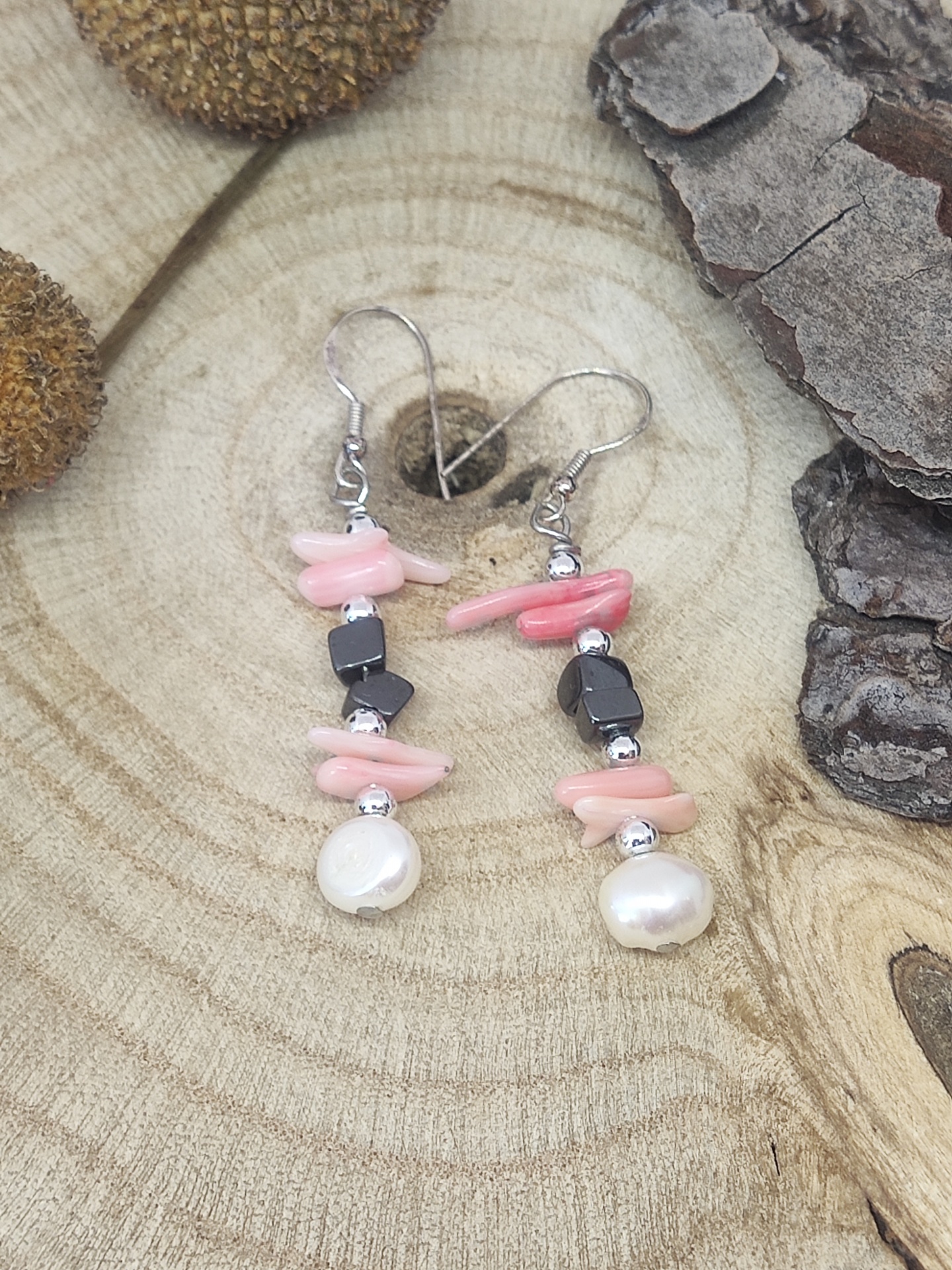 Brincos com pedras cor-de-rosa, negras e pérolas sobre madeira