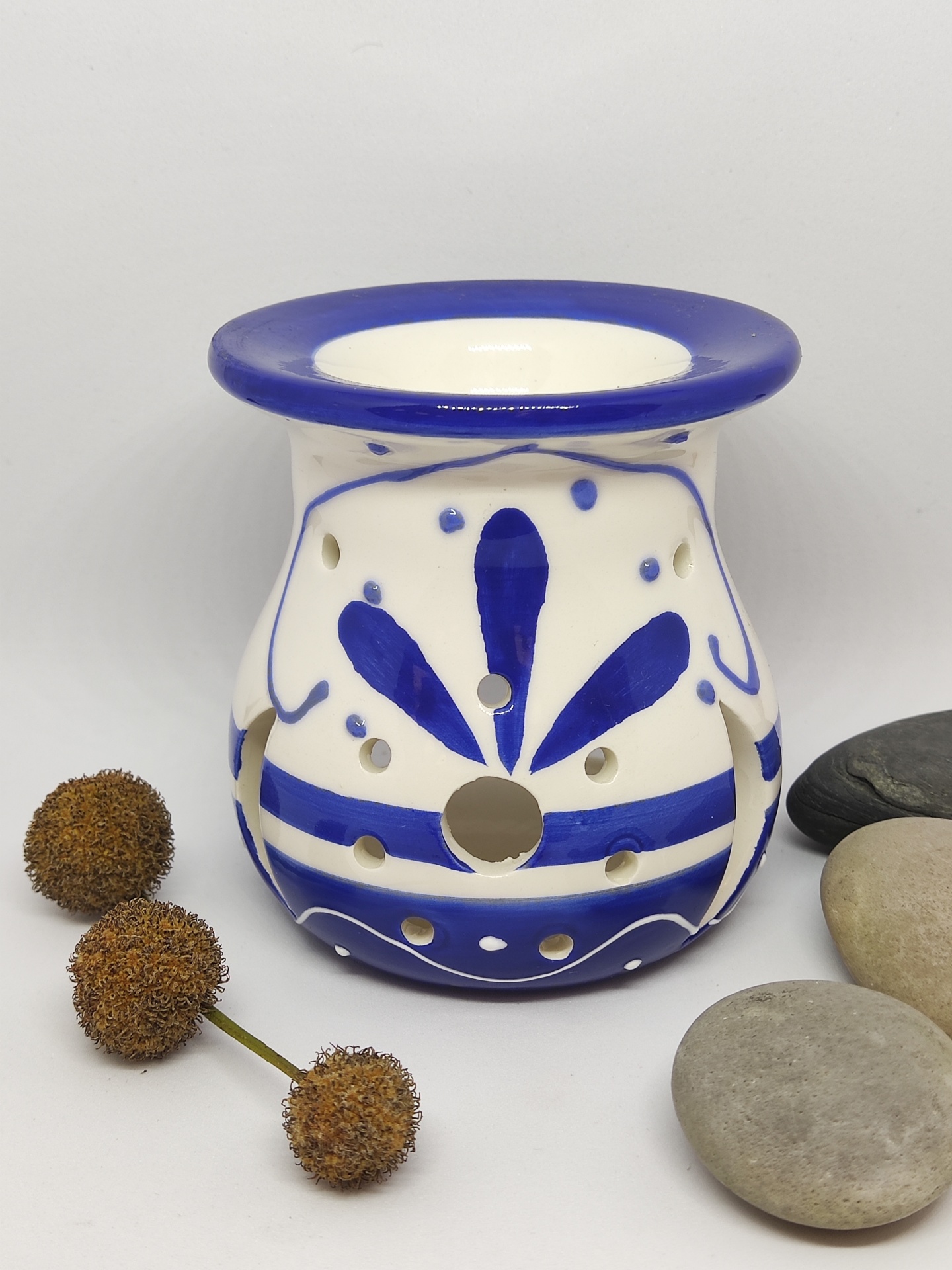 Queimador de cerâmica branco e azul com padrão floral, pedras cinzentas e vagens secas