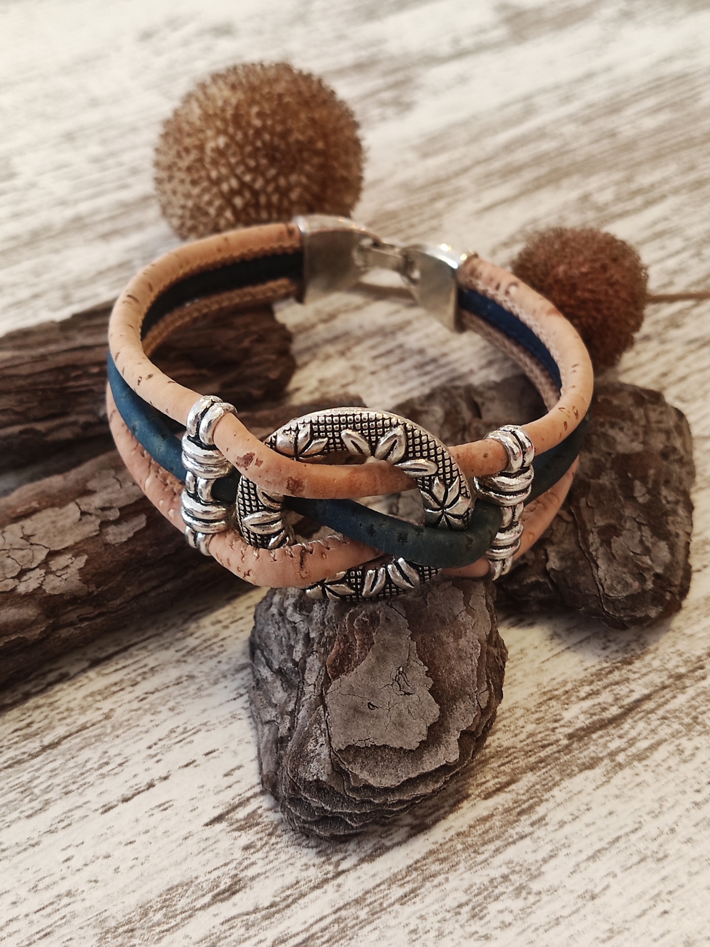 Pulseira de cortiça natural bege e azul com fecho prateado e detalhes florais sobre casca e madeira