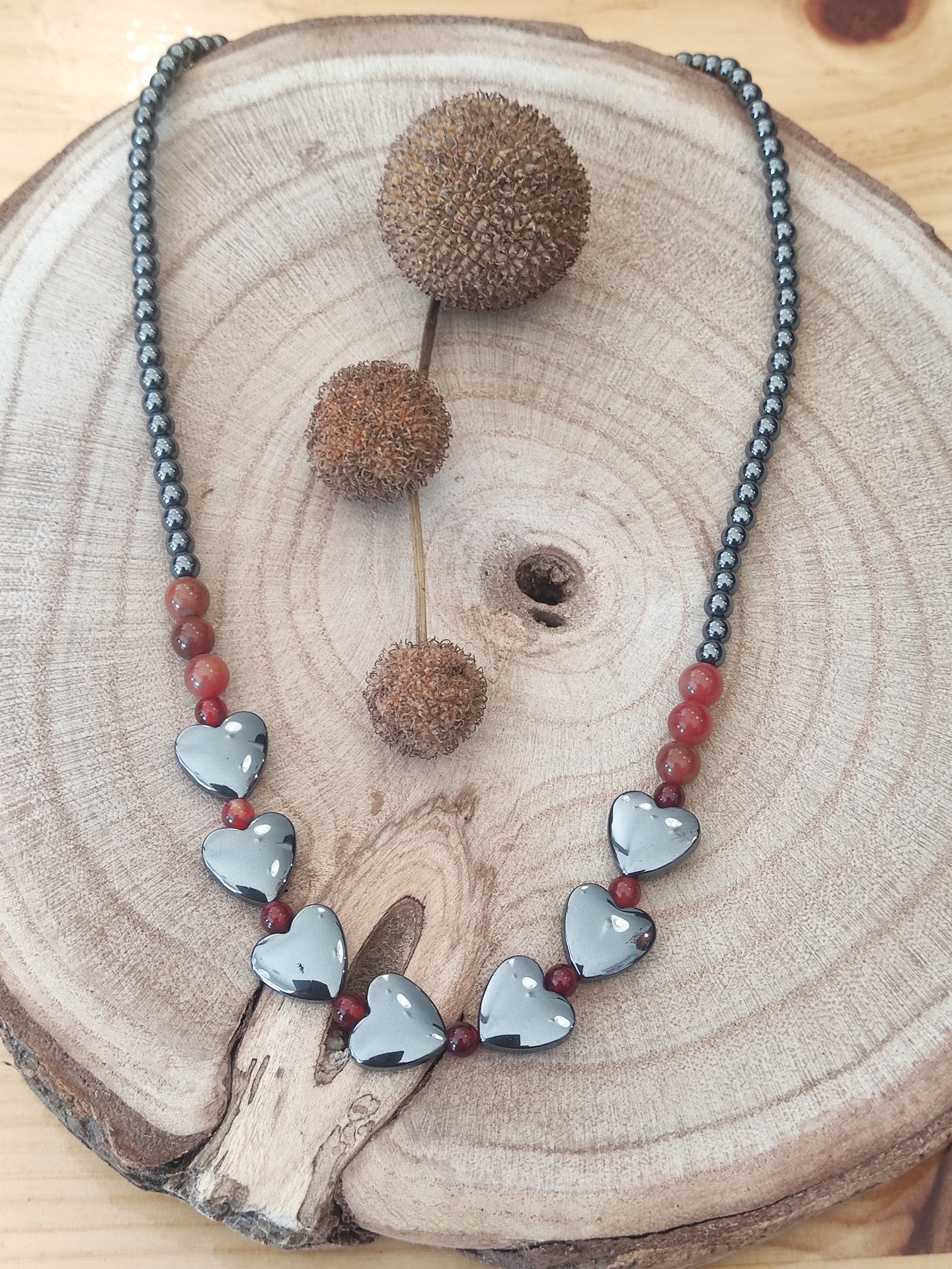 colar com contas prateadas, vermelhas e corações cinzentos sobre madeira rústica com frutos secos