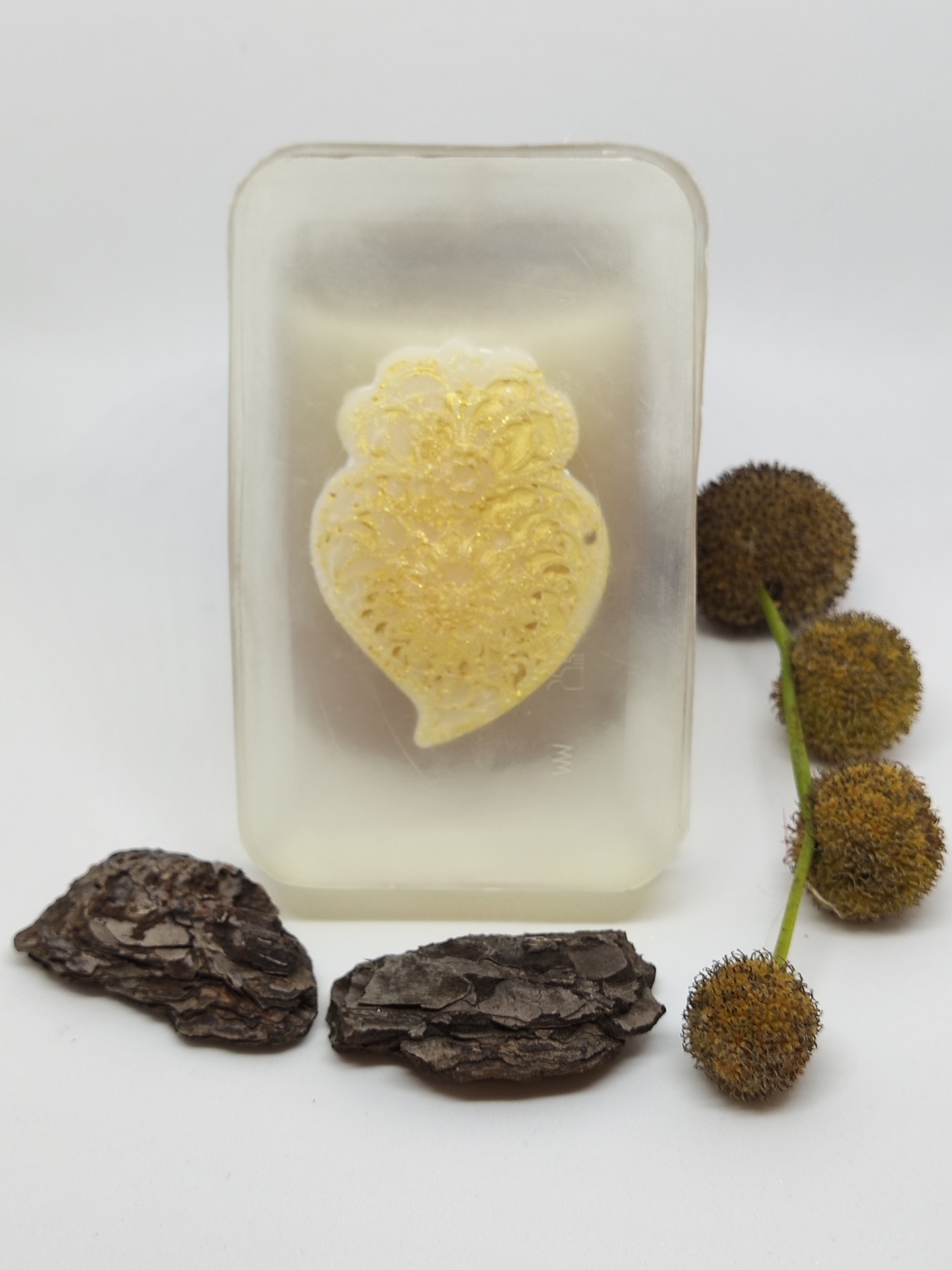Sabonete transparente com detalhe amarelo em forma de flor, casca de árvore e flores secas ao lado