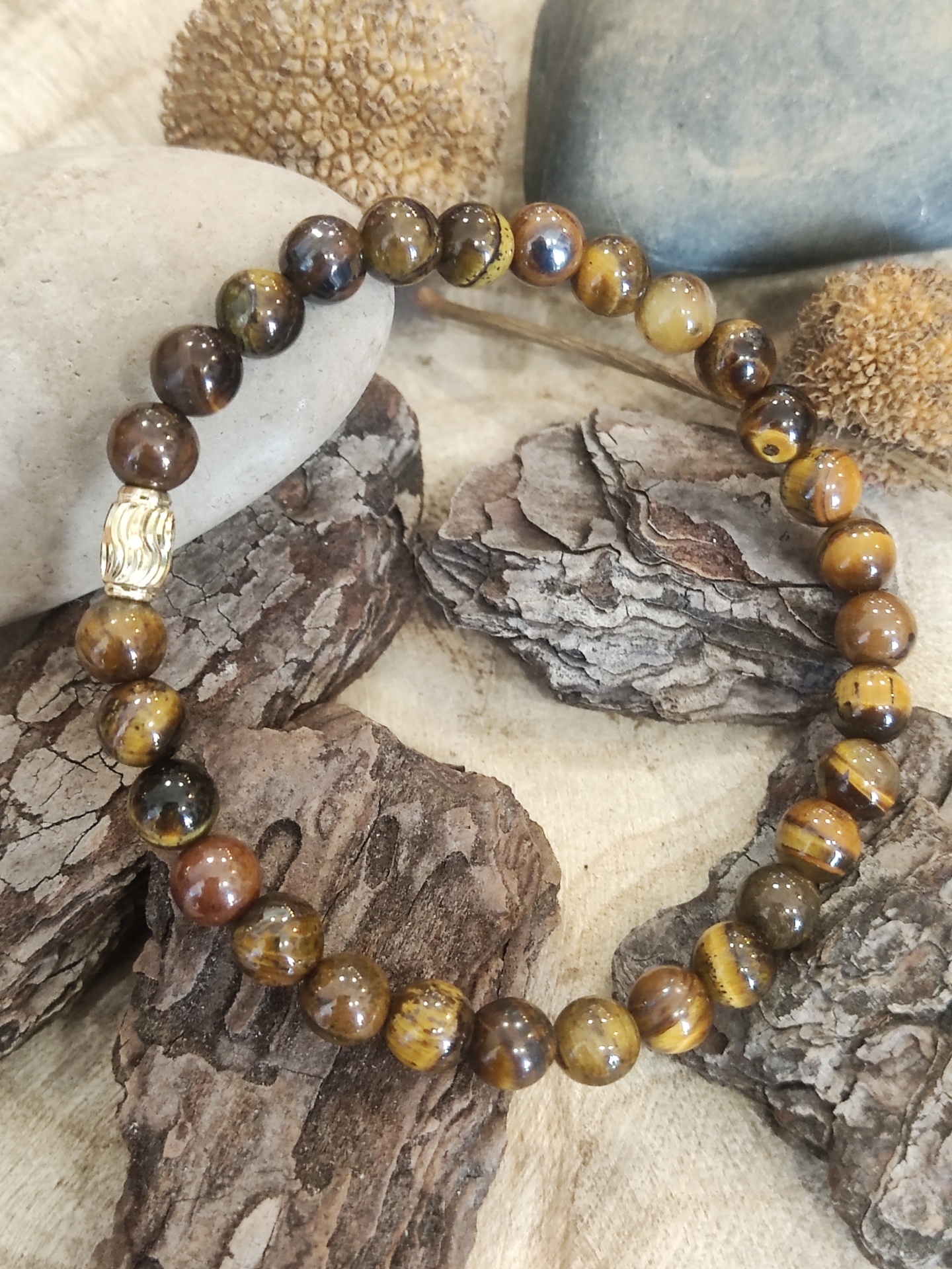 Pulseira de contas castanhas e dourada sobre cascas de madeira e pedras