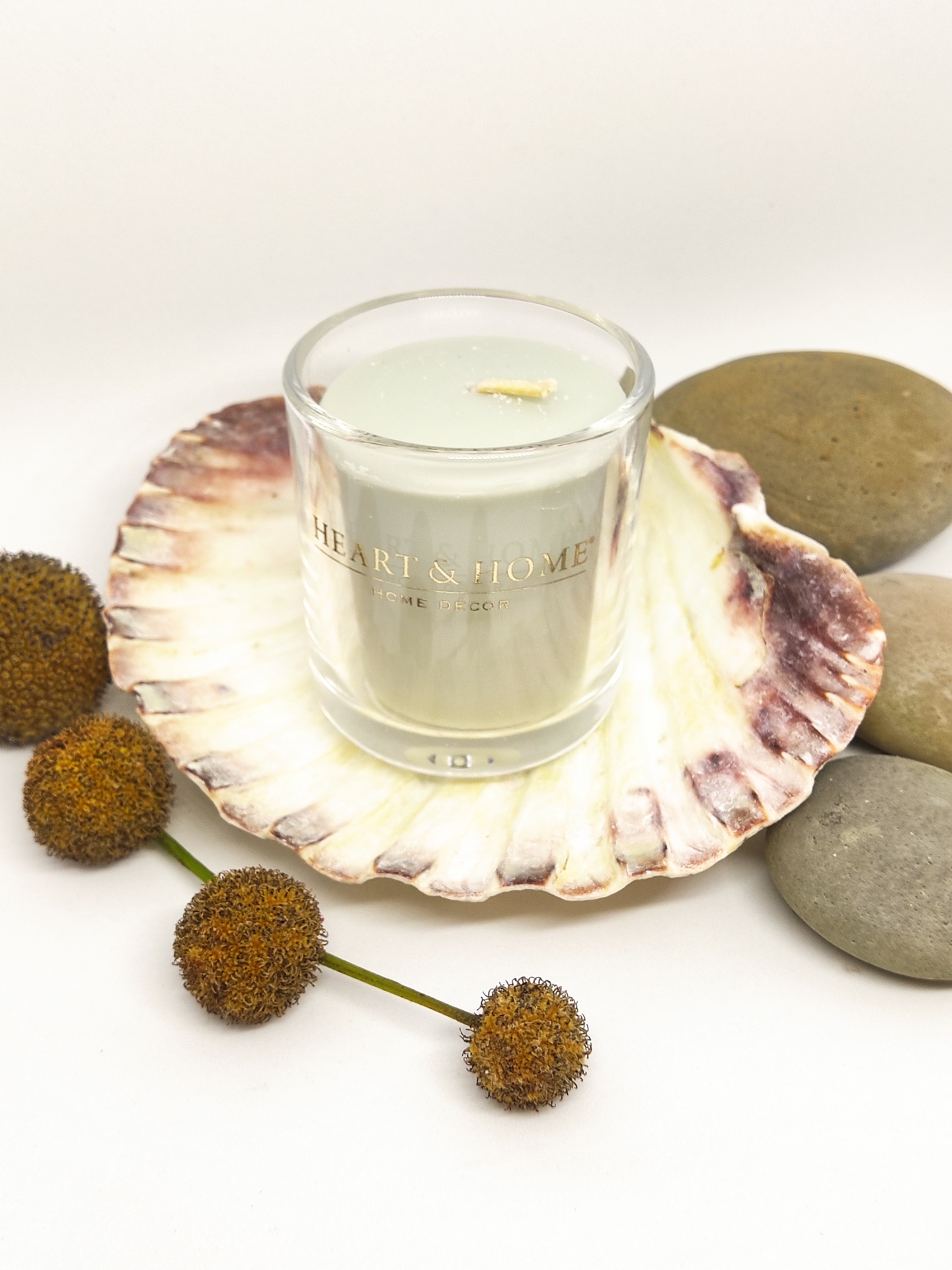 Vela branca em vidro numa concha decorativa com pedras e flores secas ao redor