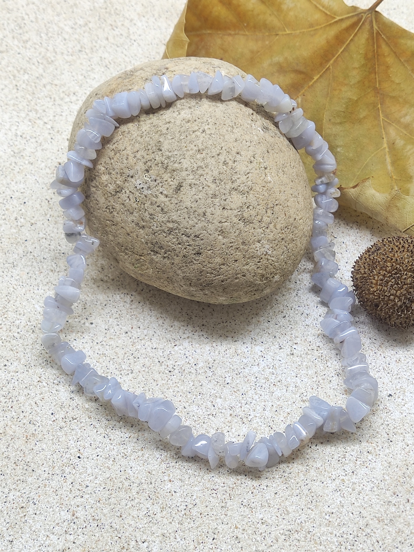 Colar de pedras azuis claras sobre pedra com folha seca a fundo