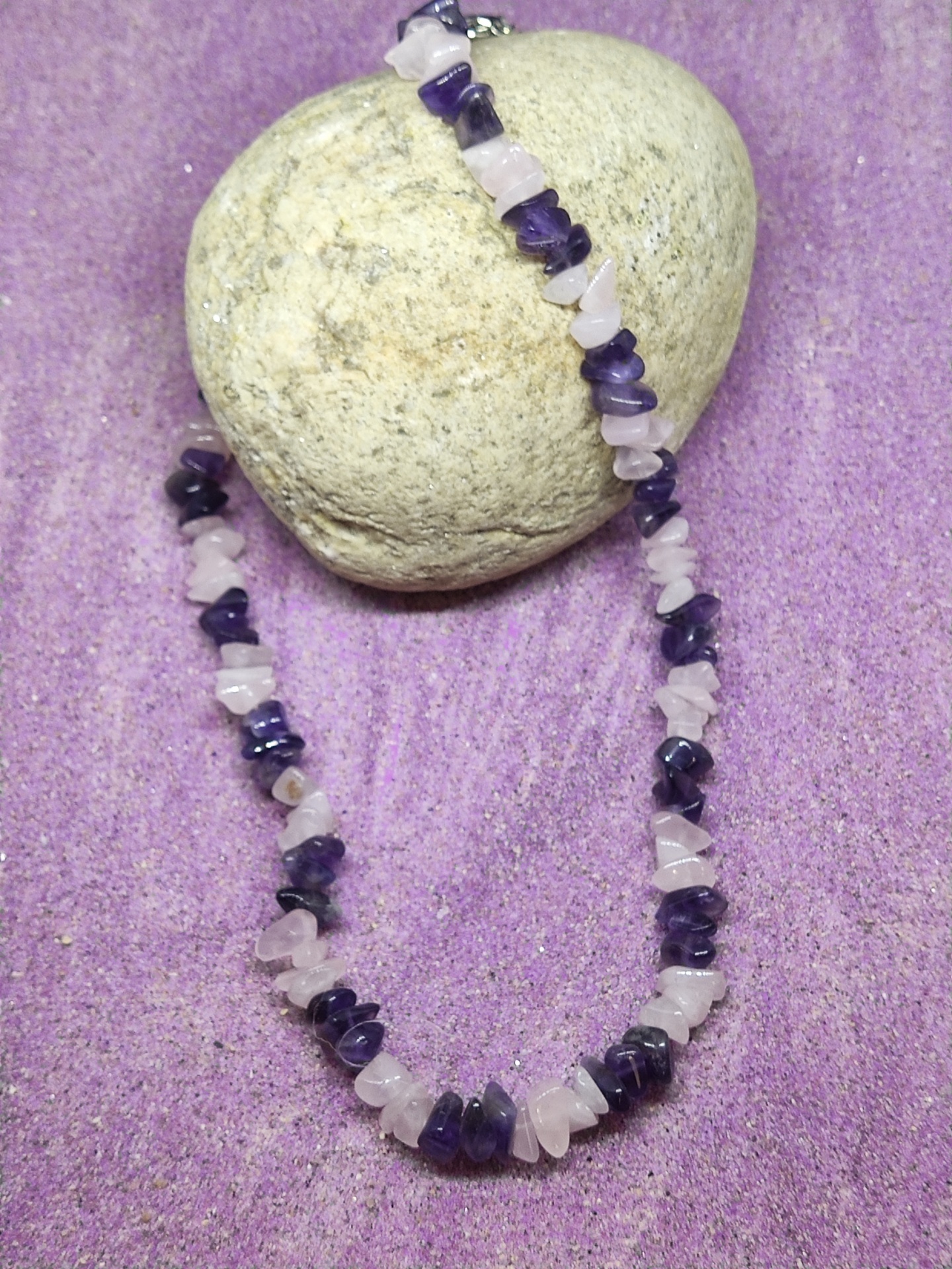 Colar de pedras naturais rosa e roxas sobre areia e pedra cinzenta