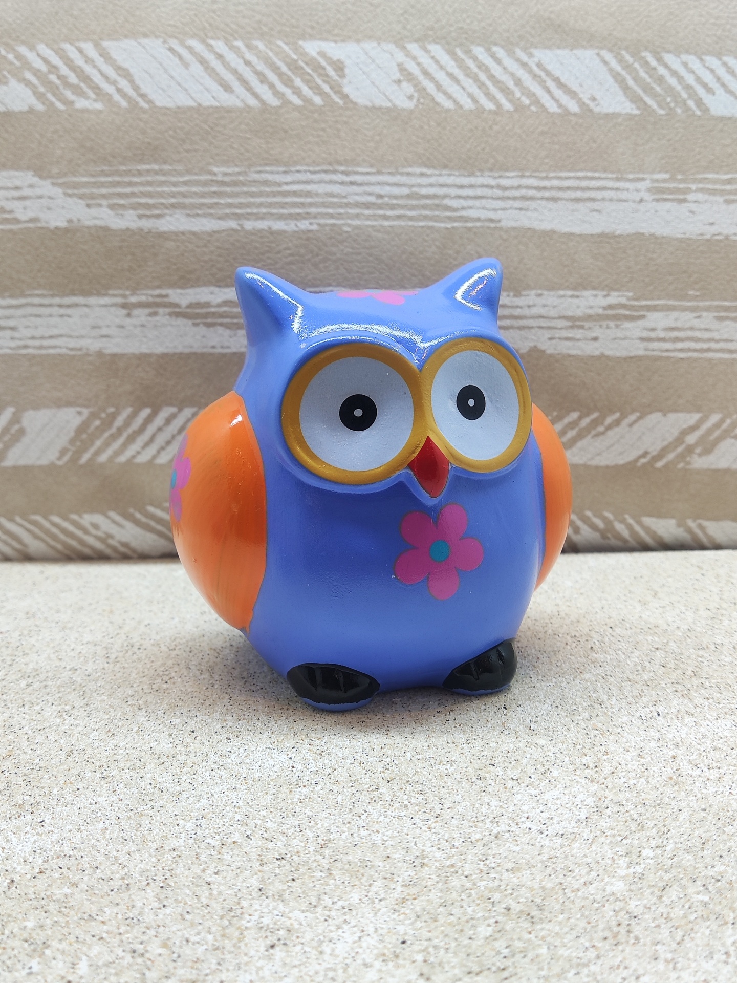 Figura de coruja azul e laranja com flores cor-de-rosa sobre superfície clara