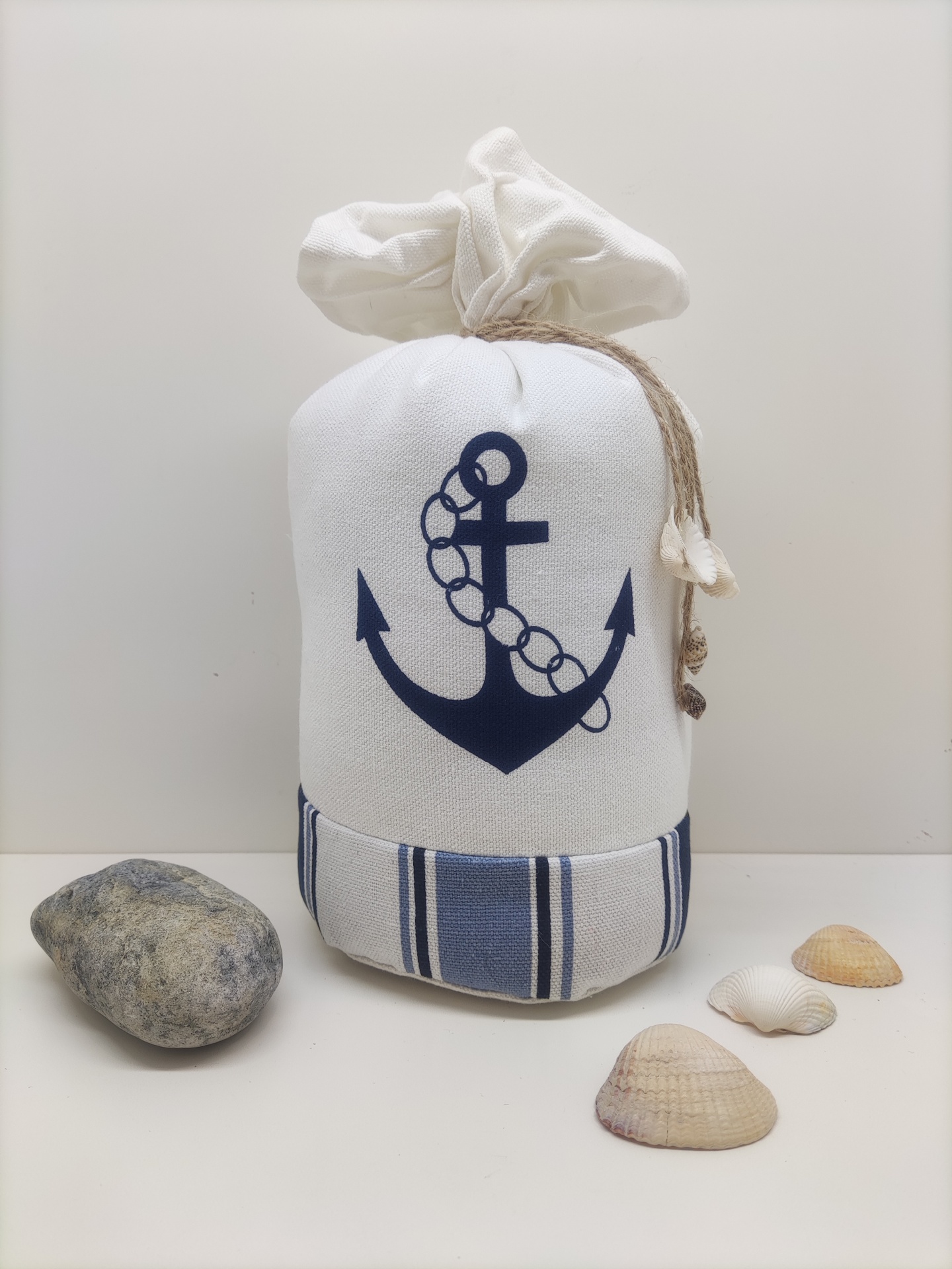 Saco branco com âncora azul e riscas azuis, pedra e conchas