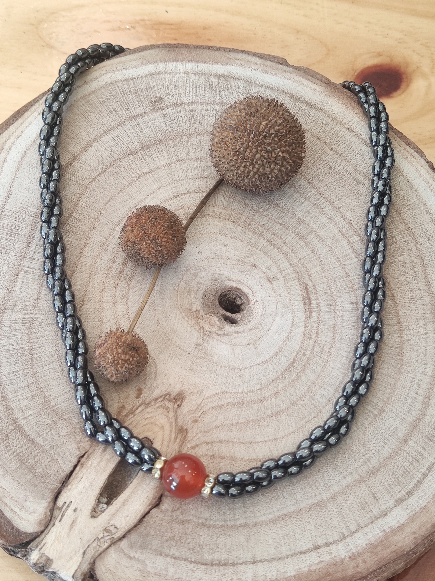 Colar preto e branco com conta vermelha sobre madeira e bolas decorativas