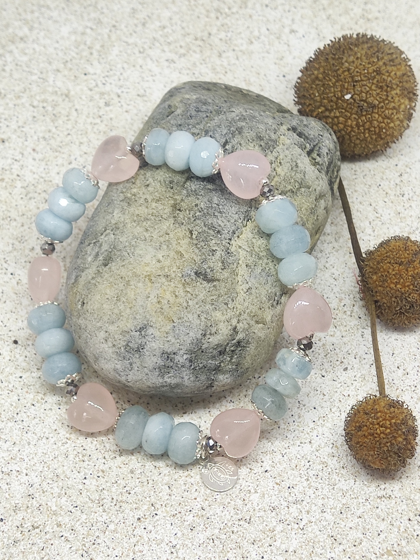 Pulseira com contas azuis e corações cor-de-rosa sobre pedra cinzenta