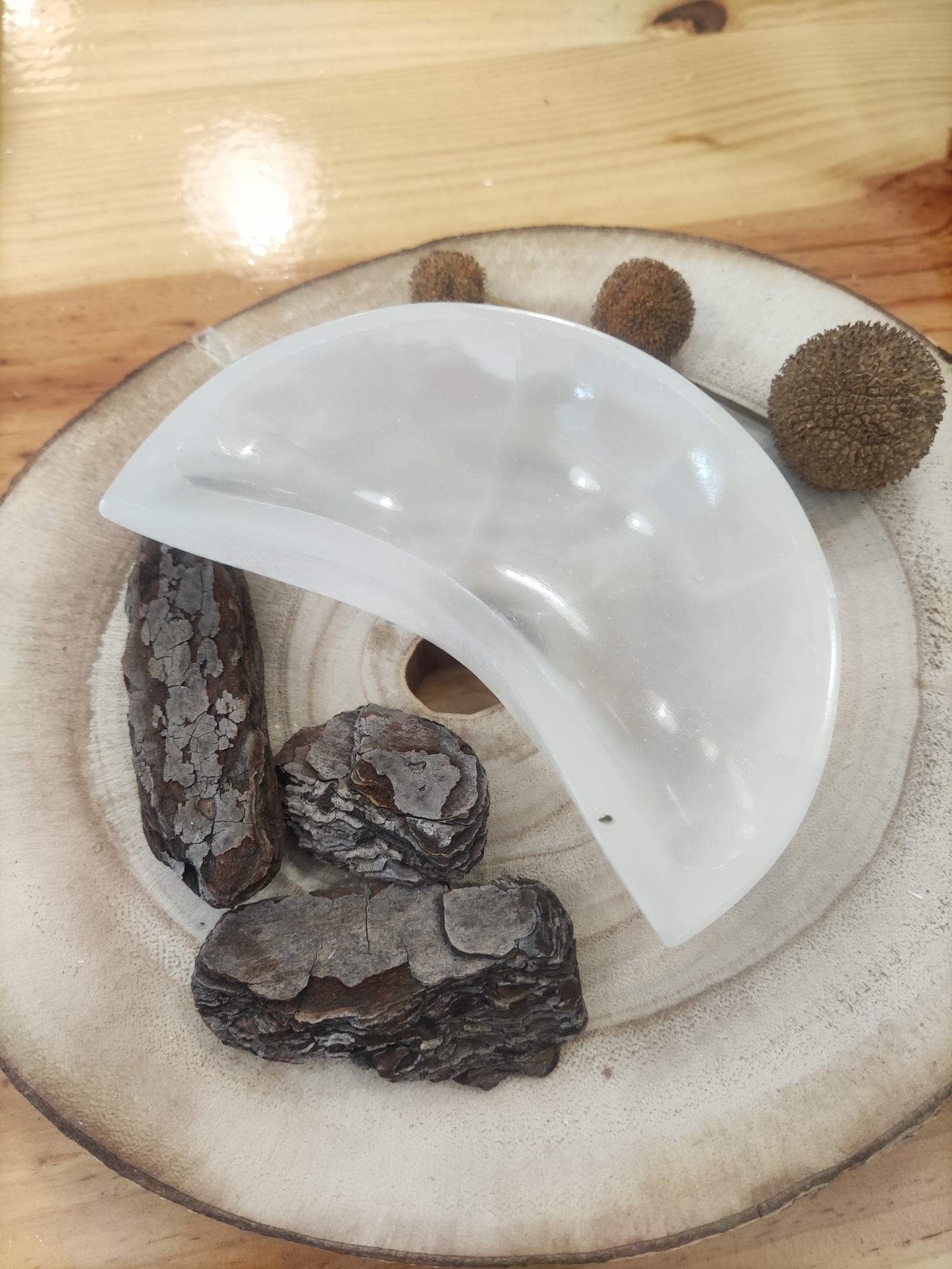 Prato branco meia-lua sobre base de madeira com cascas e bolas secas