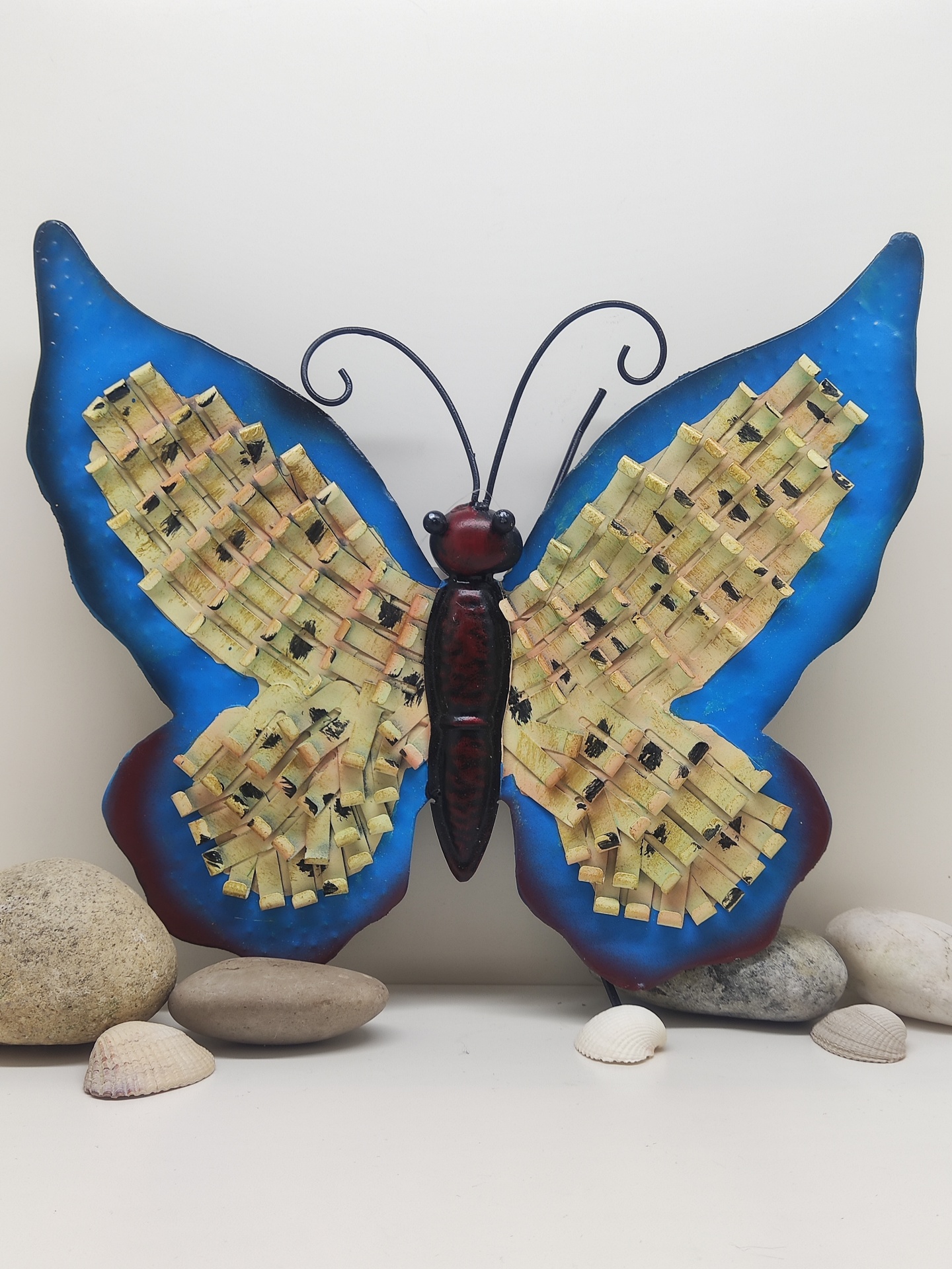 Escultura metálica de borboleta azul e amarela com pedras ao redor