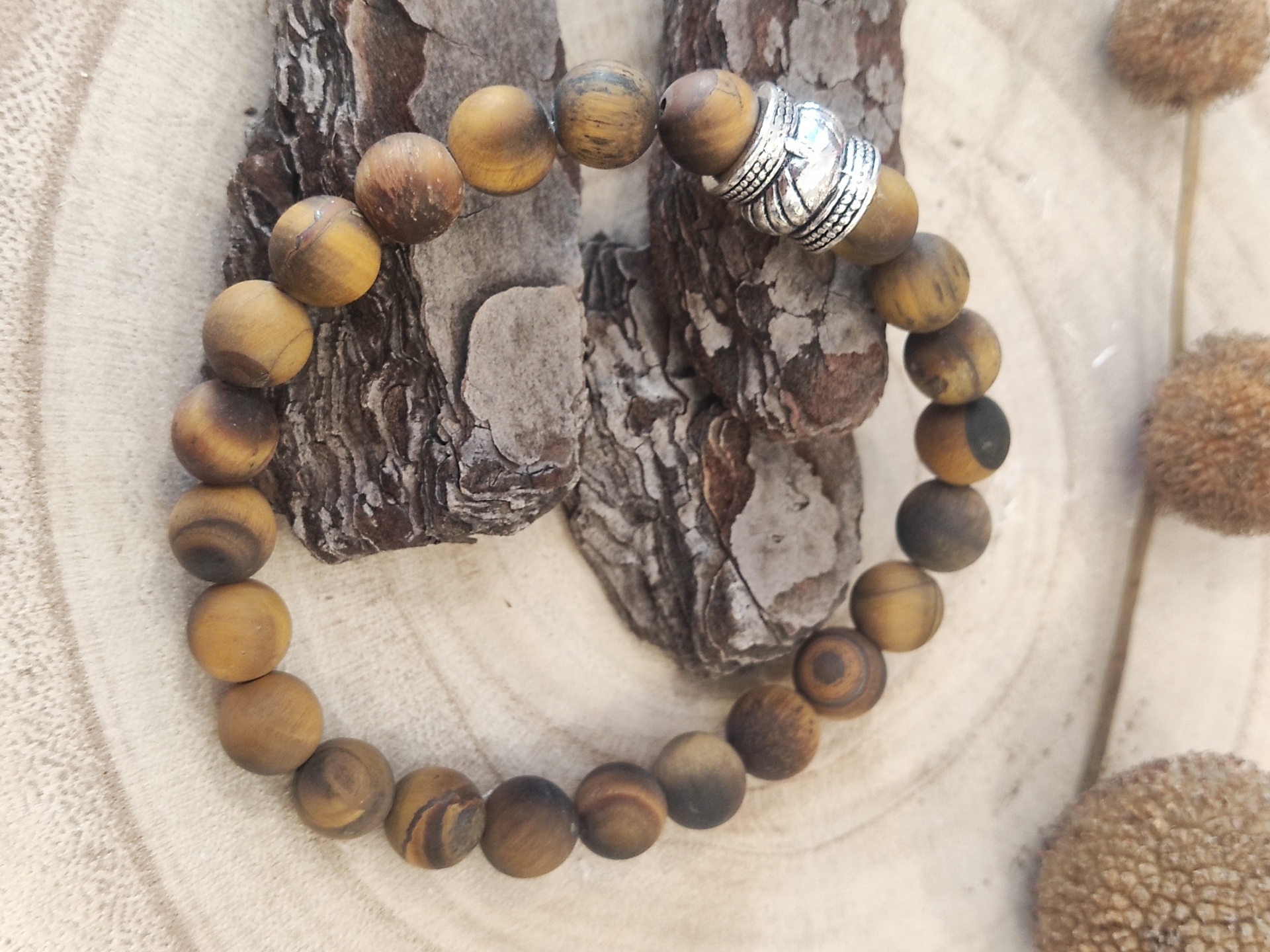 pulseira de contas de madeira castanha com detalhe metálico prateado sobre madeira clara