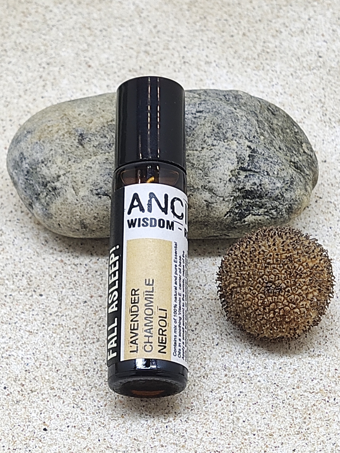 Frasco de óleo essencial próximo a pedra cinza e semente marrom sobre areia